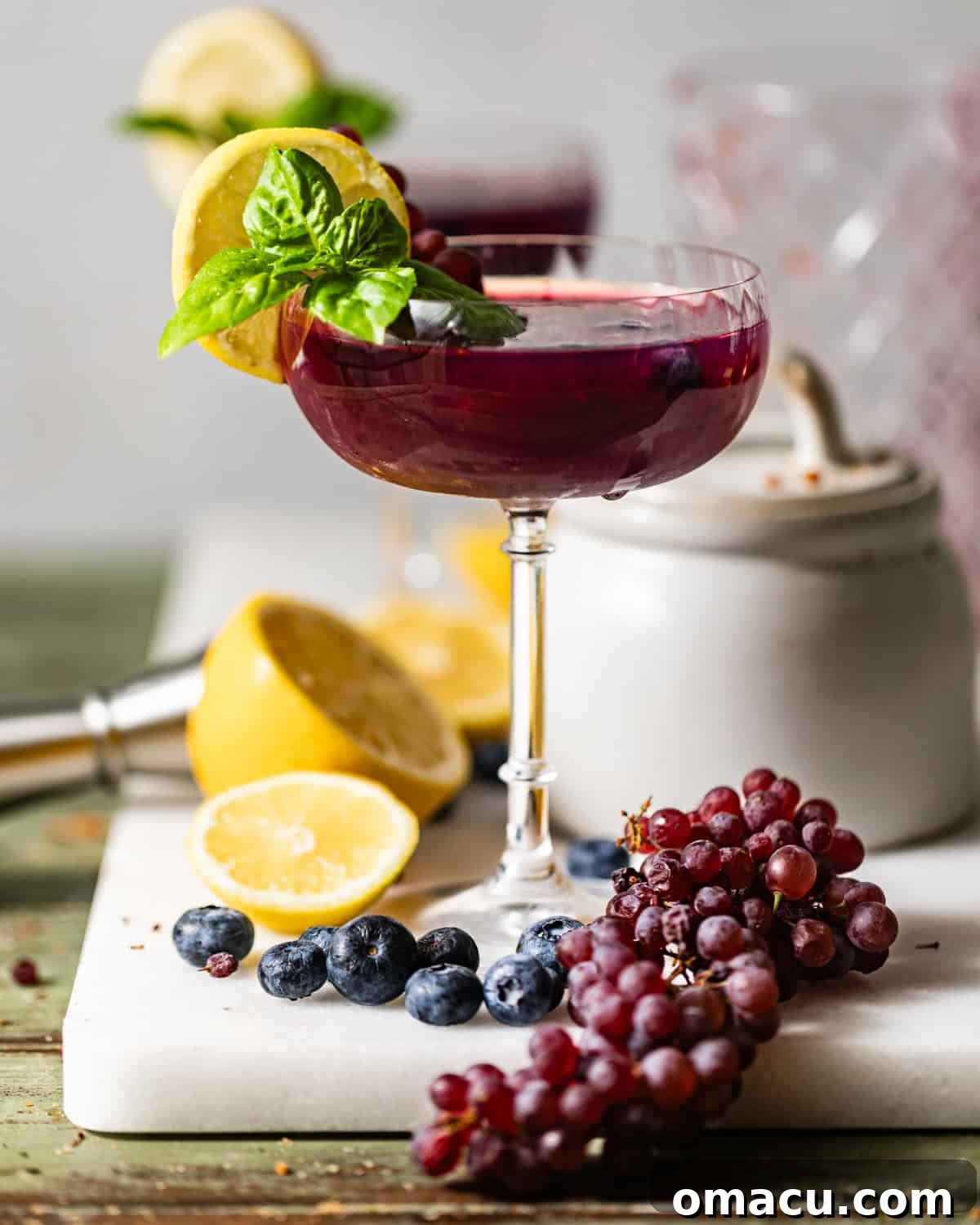 A stunning Blueberry Lemon Drop Martini on a white serving tray, beautifully garnished with fresh blueberries, lemon slices, and grapes, inviting a perfect summer sip.