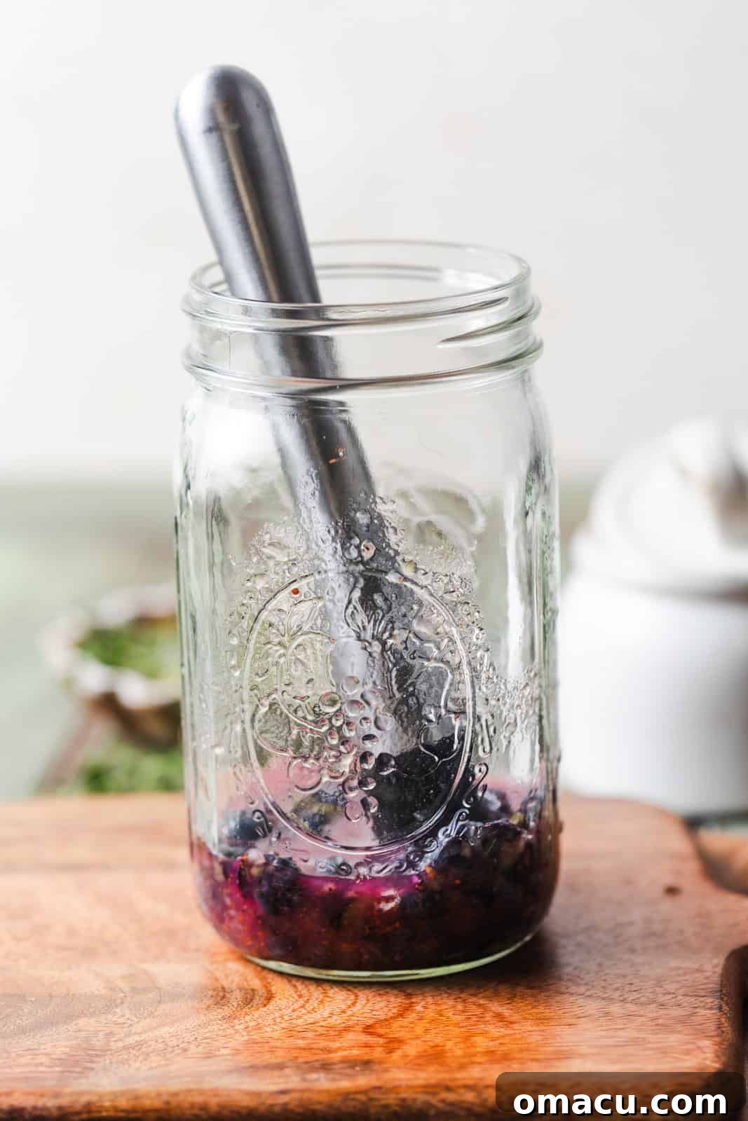 Fresh blueberries, rich blueberry preserves, and vibrant lemon juice carefully placed in a large mason jar, ready for muddling to release their full flavors.