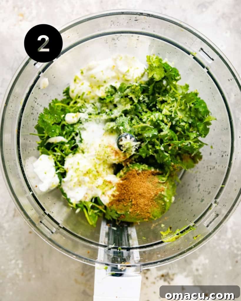 All avocado crema ingredients, including avocado, sour cream, lime juice, garlic, cilantro, cumin, and salt, placed in a food processor ready for blending.