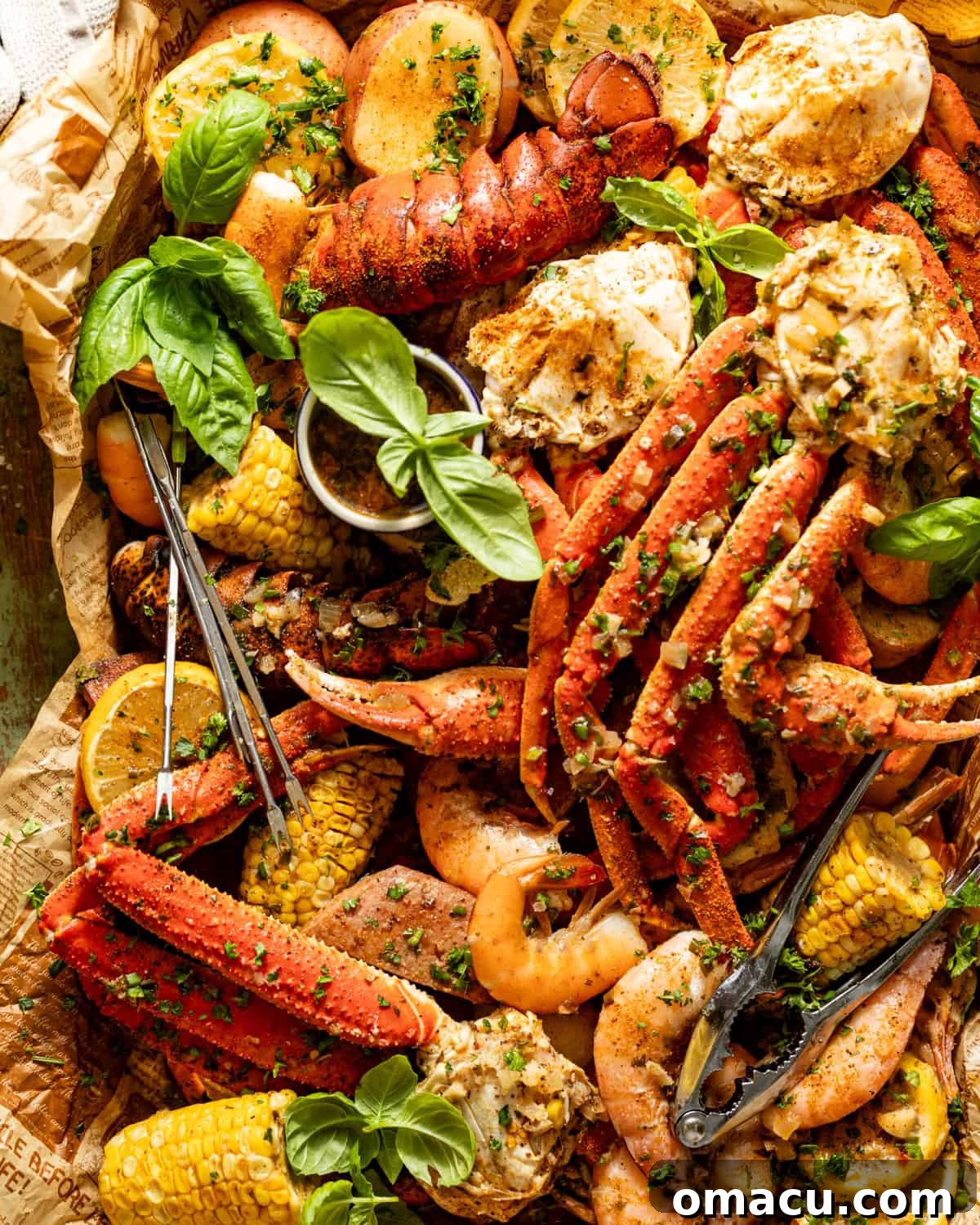 A bountiful seafood boil in a bag spread on a baking sheet, featuring crab legs, shrimp, lobster, corn, sausage, and potatoes, garnished with fresh basil and garlic butter sauce.