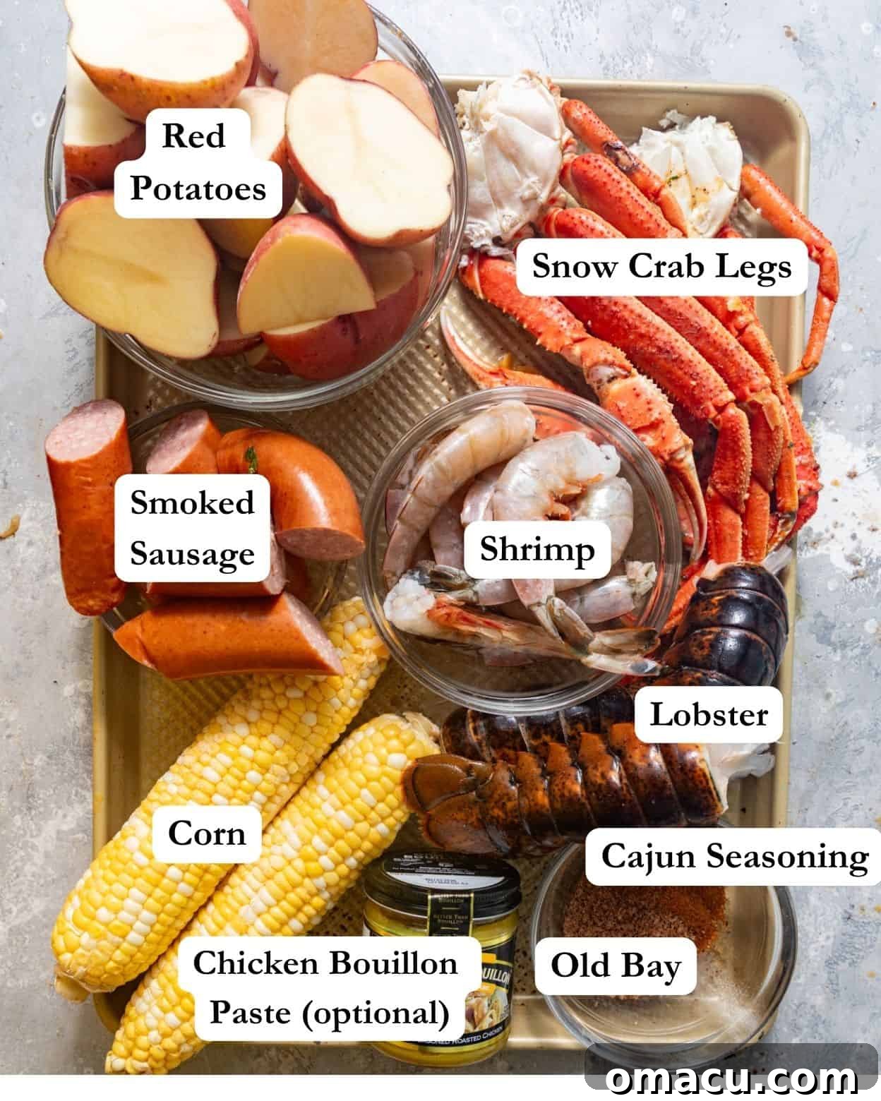 Ingredients for seafood boil in a bag laid out: snow crab legs, lobster, smoked sausage, corn, shrimp, Old Bay, Cajun seasoning, chicken bouillon paste, and red potatoes.