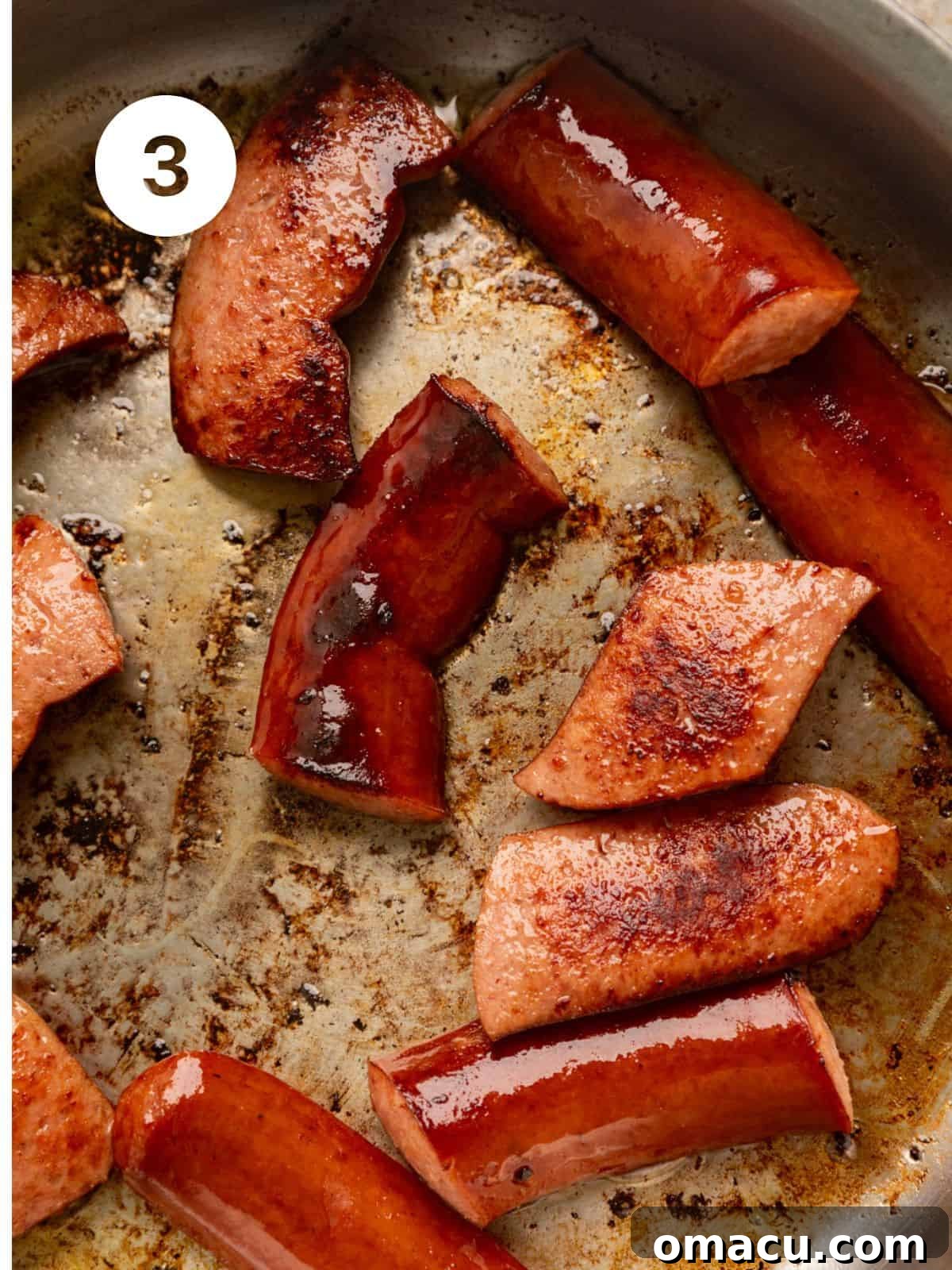 Smoked Andouille sausage pieces browning in a skillet on the stove.