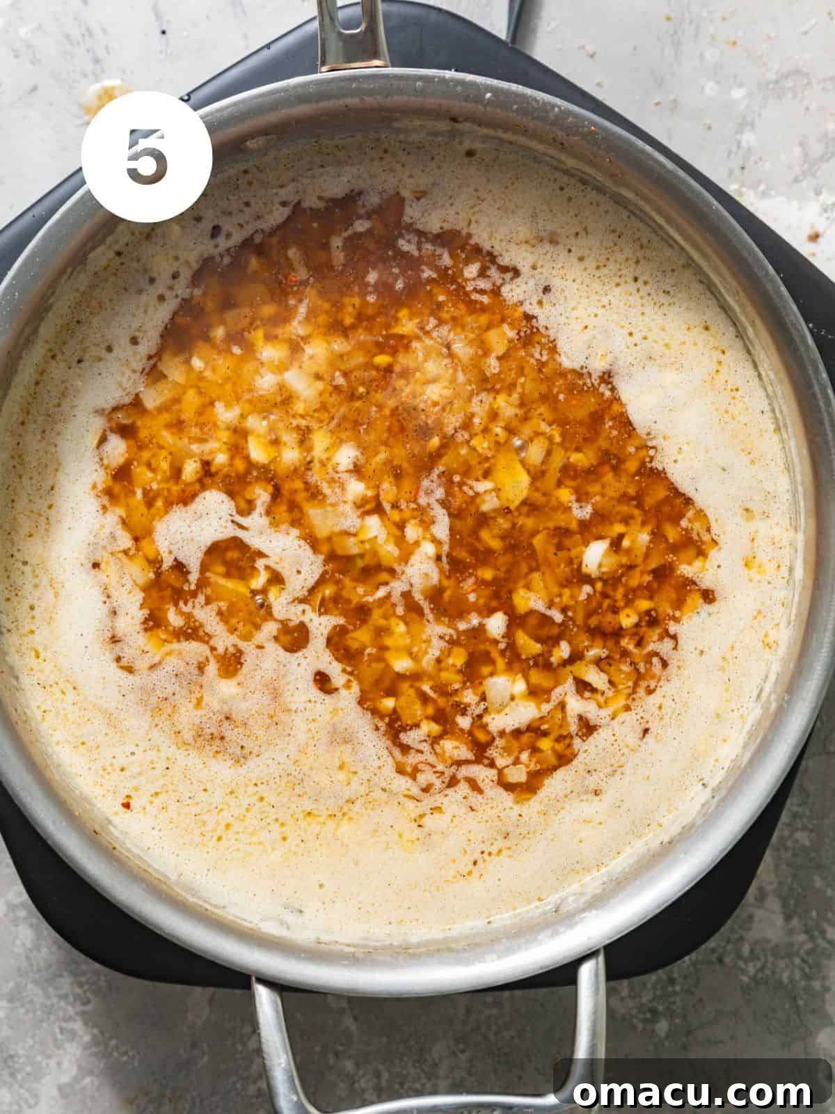 Seafood boil sauce simmering in a skillet with onions, garlic, and a blend of vibrant seasonings.