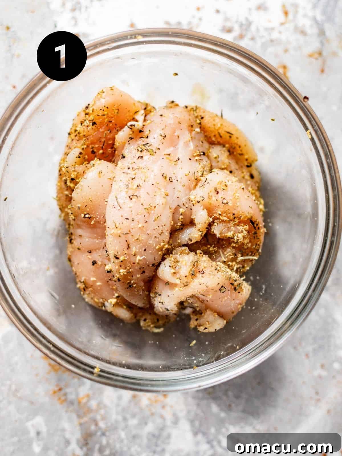 Chicken tenderloins seasoned with spices in a stainless steel bowl, ready for the breading process.