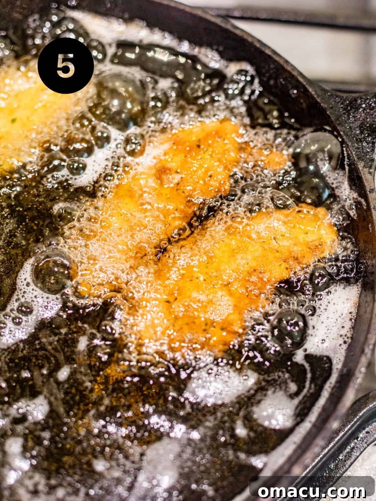 Several chicken tenderloins being deep-fried in hot oil, achieving a perfect golden-brown color.