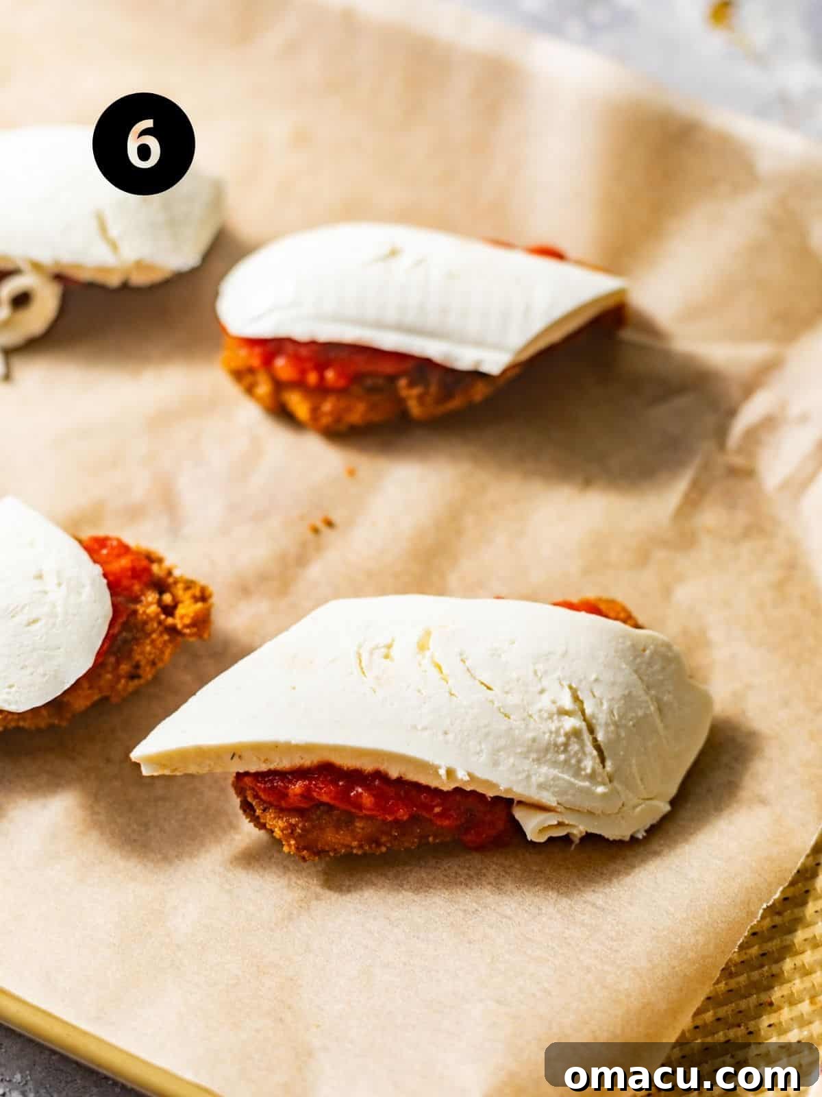 Two fried chicken cutlets on a baking tray, generously topped with marinara sauce and slices of fresh mozzarella cheese, poised for broiling.