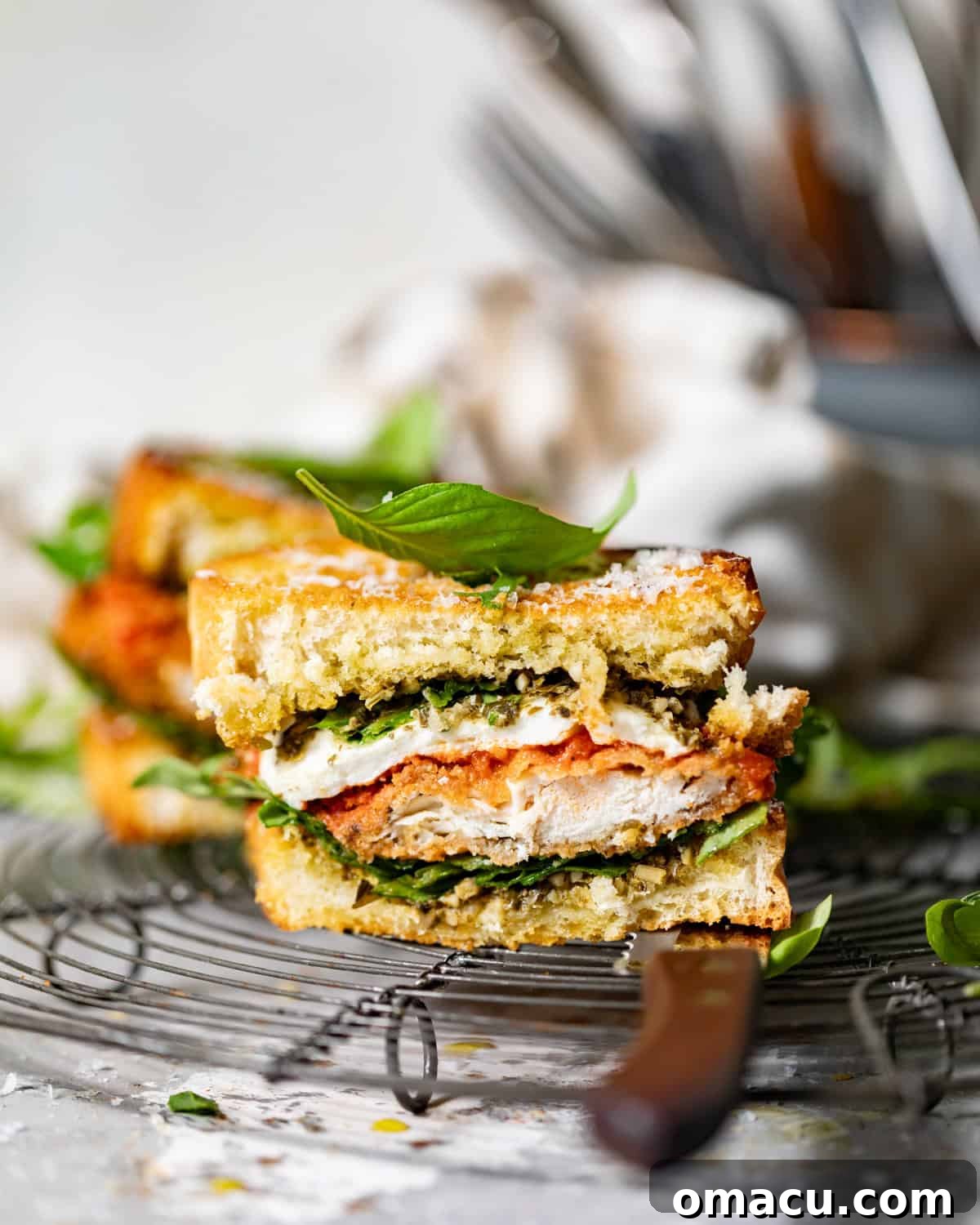A perfectly assembled and sliced chicken parmesan sandwich on a wire rack, showcasing the layers of crispy chicken, melted cheese, and fresh greens.
