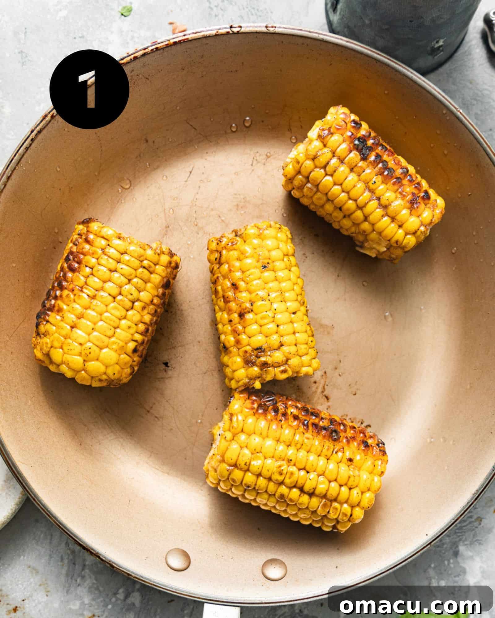 Ears of corn being sautéed in a skillet with olive oil, developing a golden-brown hue.