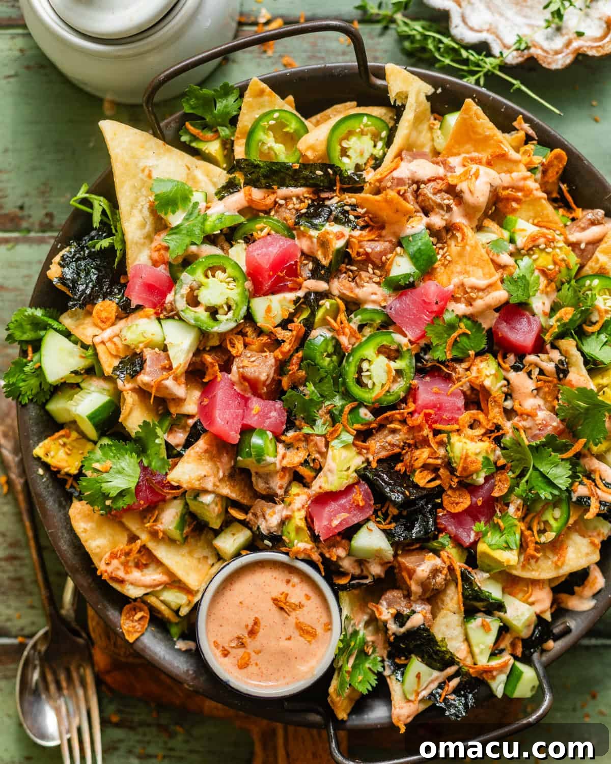 Vibrant Poke Nachos on a serving dish, generously topped with thinly sliced jalapenos, crispy garlic, fresh cucumbers, sesame seeds, and a creamy swirl of homemade yum yum sauce, ready to be enjoyed.