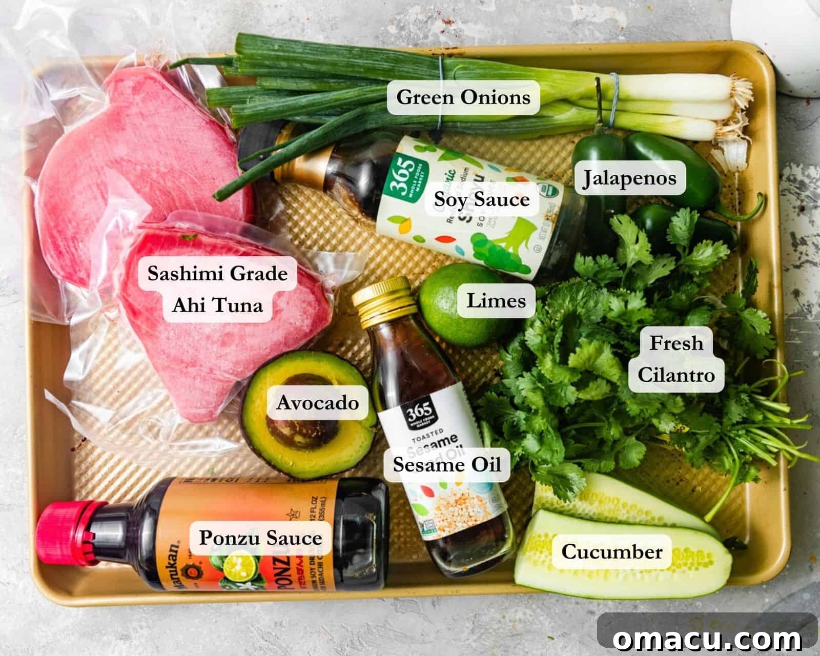 A vibrant selection of ingredients for homemade Poke Nachos laid out on a baking sheet, including fresh cubes of ahi tuna, whole limes, a bottle of soy sauce, a bottle of ponzu sauce, fresh cilantro, cucumber slices, green onions, sliced jalapenos, and a perfectly ripe avocado, all ready for preparation.