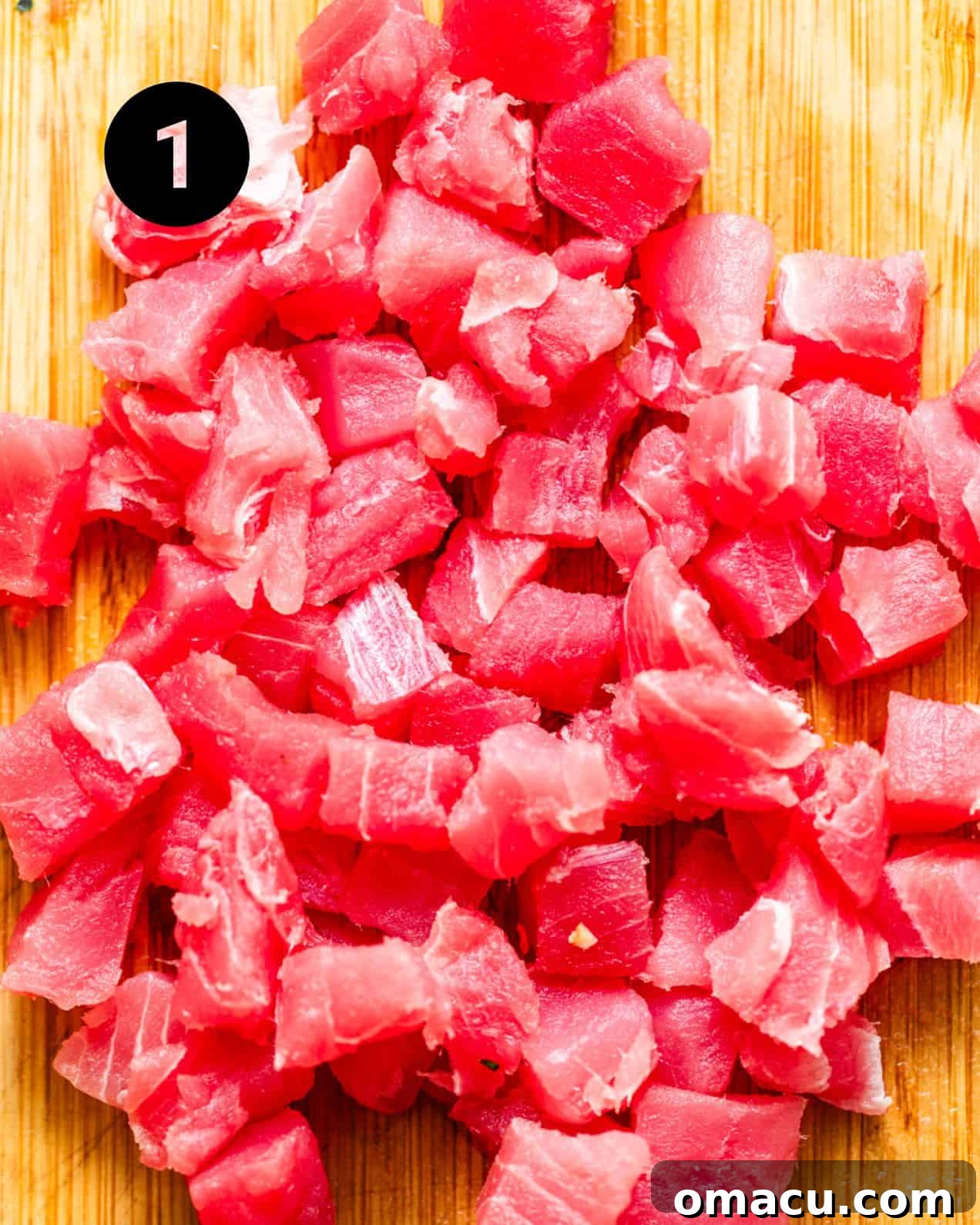 Fresh ahi tuna on a cutting board, expertly cut into uniform chunks, ready for marinating.