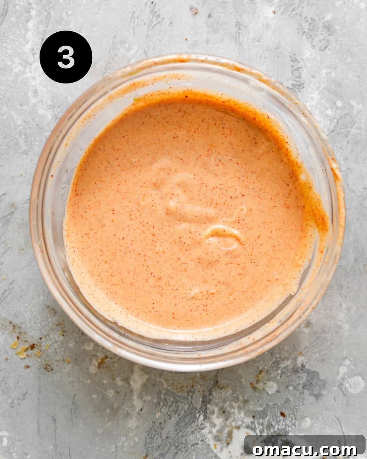 A creamy, pale orange yum yum sauce, perfectly whisked and smooth, in a glass bowl.