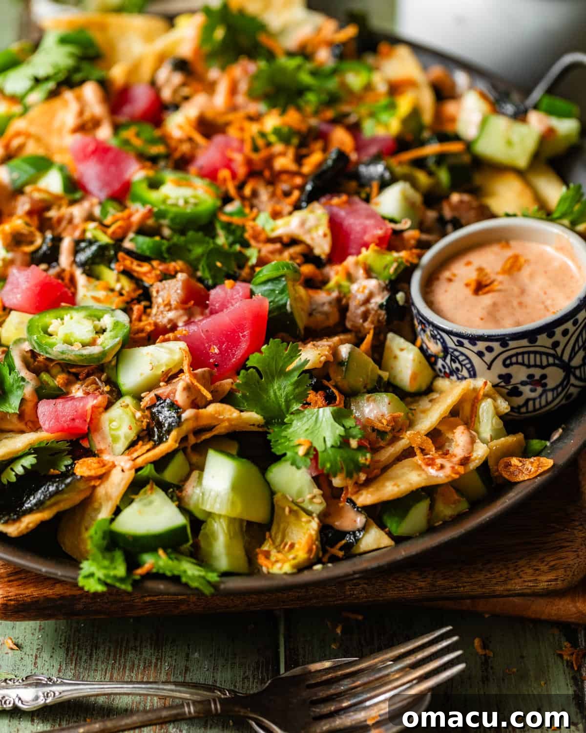 A stunning platter of poke nachos beautifully arranged, positioned next to a small bowl of extra yum yum sauce for dipping, ready to be enjoyed.