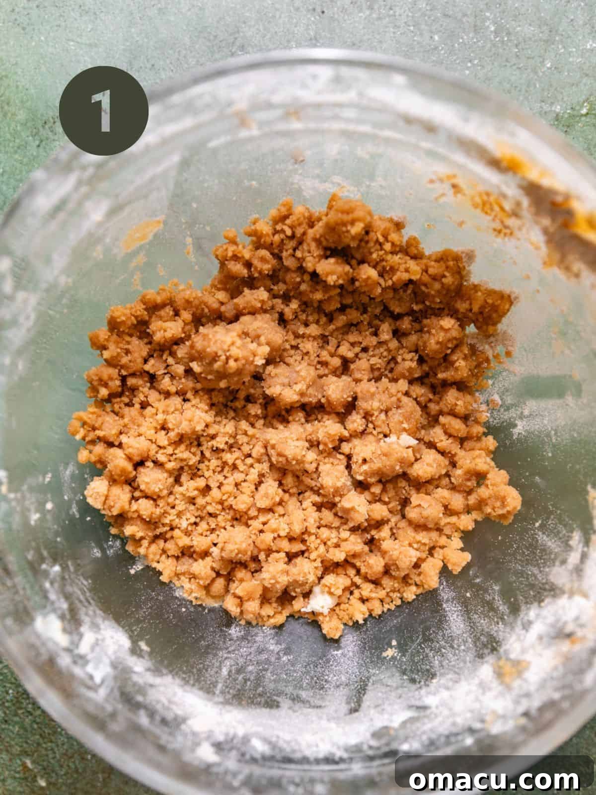 Close-up of cinnamon streusel mixture in a glass mixing bowl, showing crumbly texture.