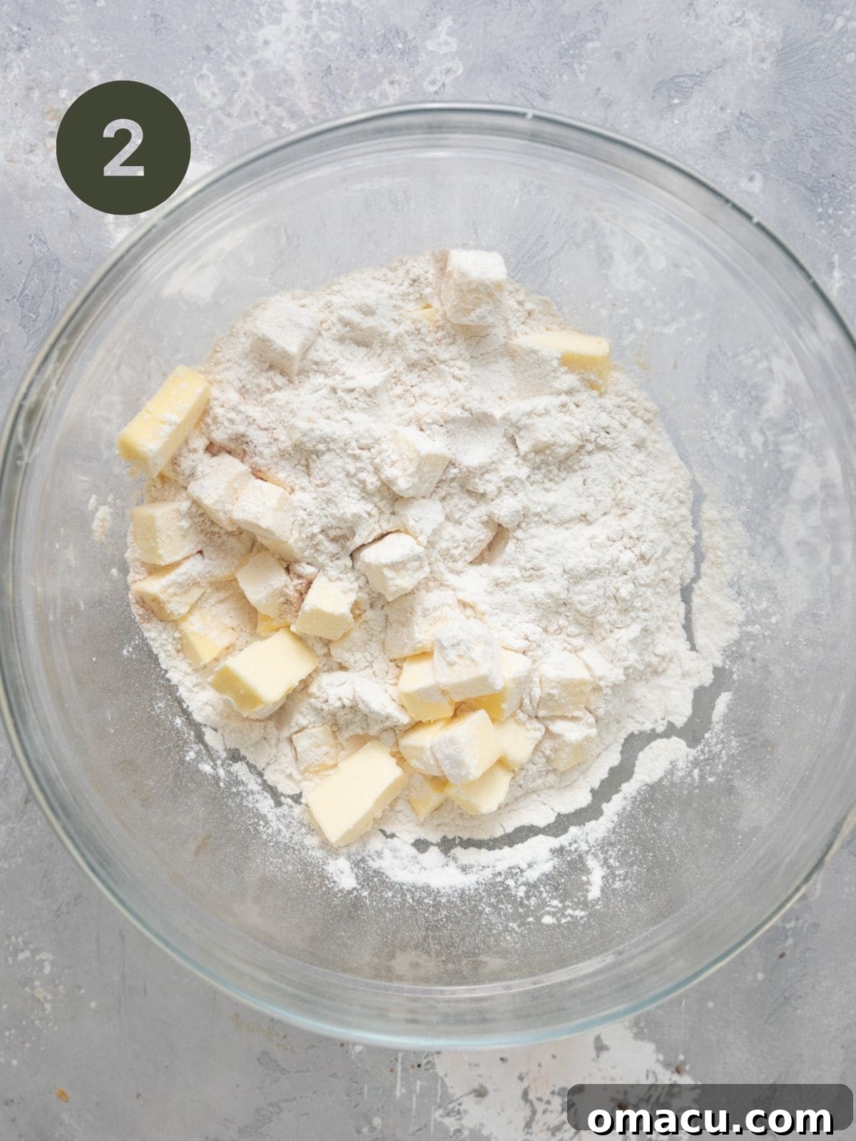 Flour, baking powder, cinnamon, salt, and cold cubed butter being mixed by hand in a bowl for the biscuit topping.