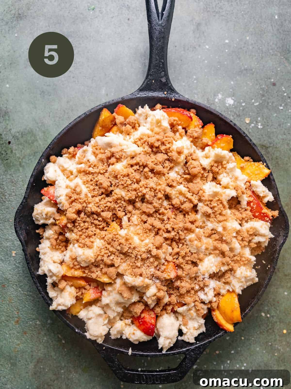 Cast iron skillet filled with peach mixture, topped with clumps of biscuit dough and a sprinkle of cinnamon streusel.
