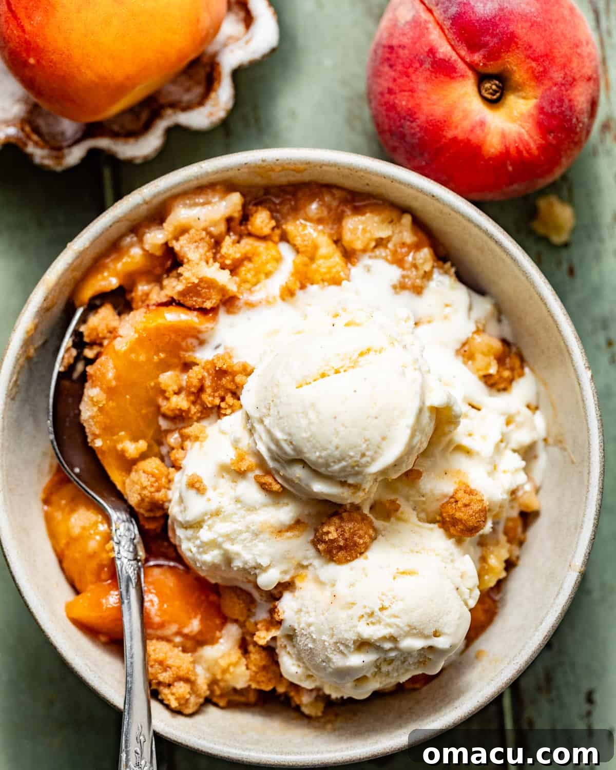 Warm peach cobbler in a bowl topped with two scoops of vanilla ice cream.
