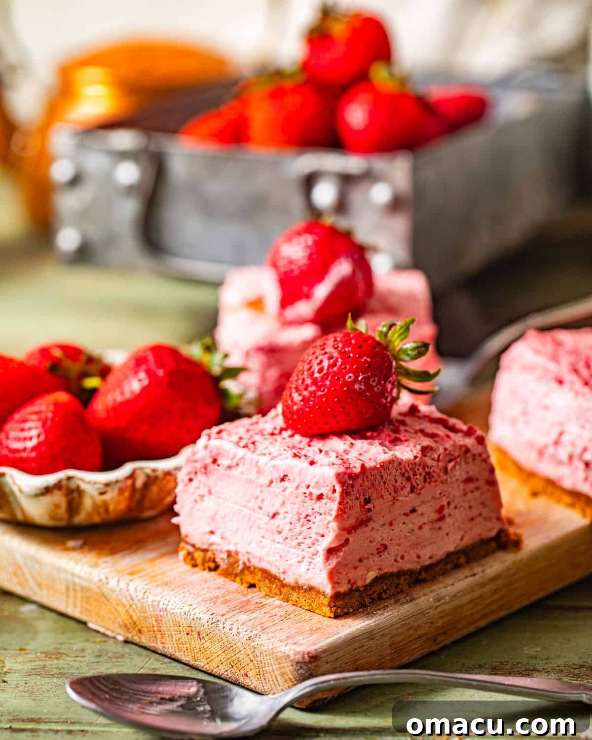 strawberry cheesecake bars on a serving board with fresh cut strawberries on top. 