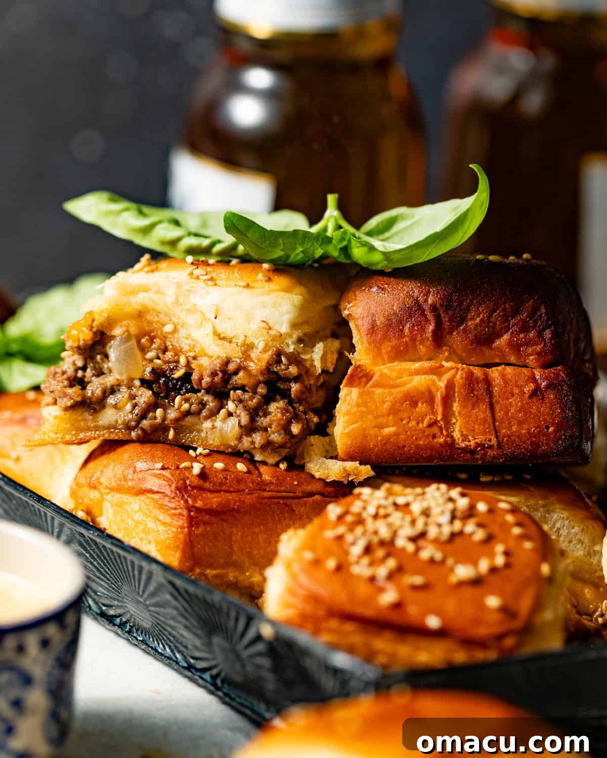 A baking sheet filled with golden-brown cheeseburger sliders, garnished with sesame seeds and fresh basil, fresh out of the oven.