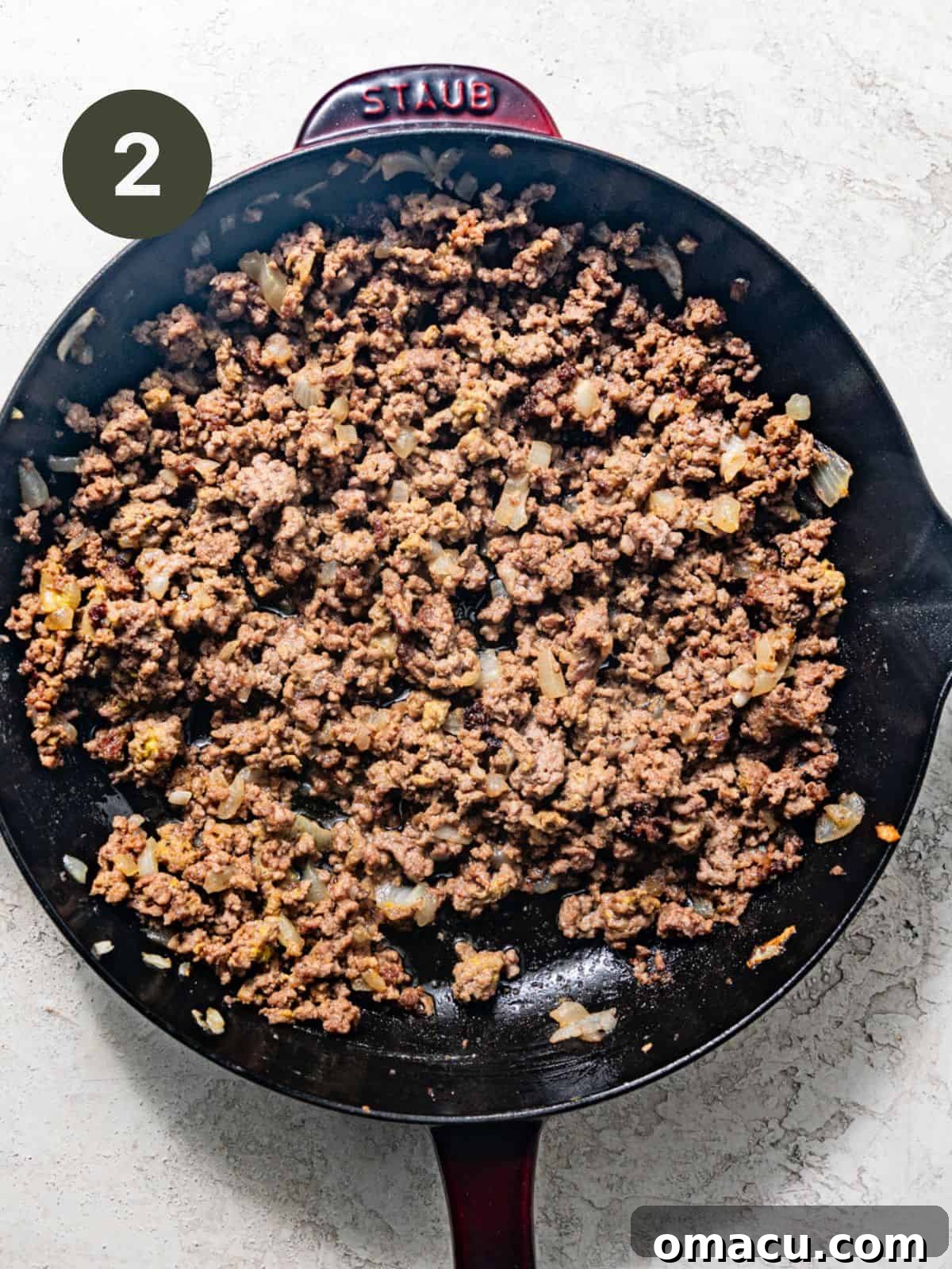 Ground beef, diced onions, and various seasonings cooking in a large skillet over medium heat, browning nicely.
