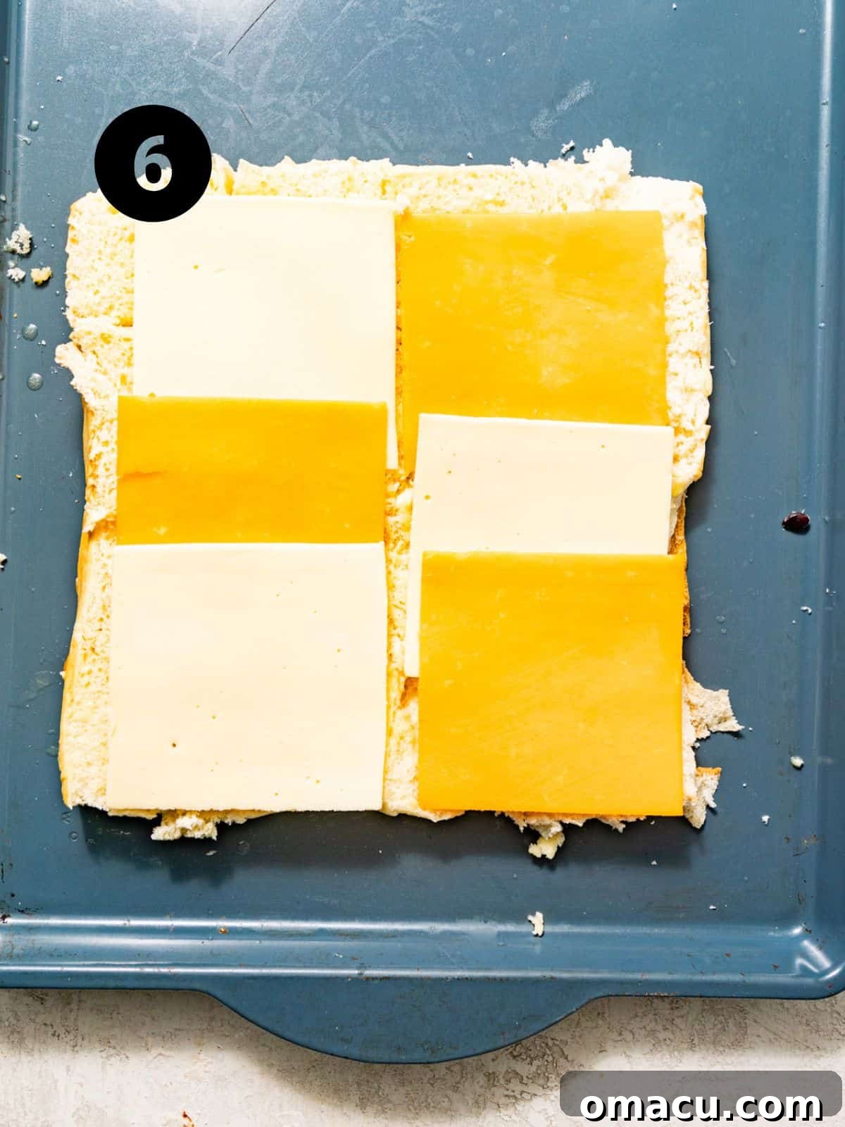Slices of American and cheddar cheese laid evenly across the bottom halves of the Hawaiian rolls on a baking sheet.