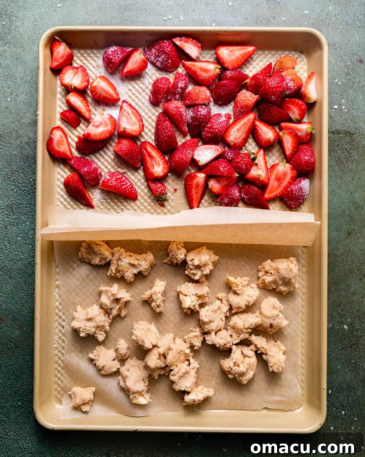 Fresh strawberries and pieces of shortcake dough arranged on a parchment-lined baking sheet, ready for roasting.