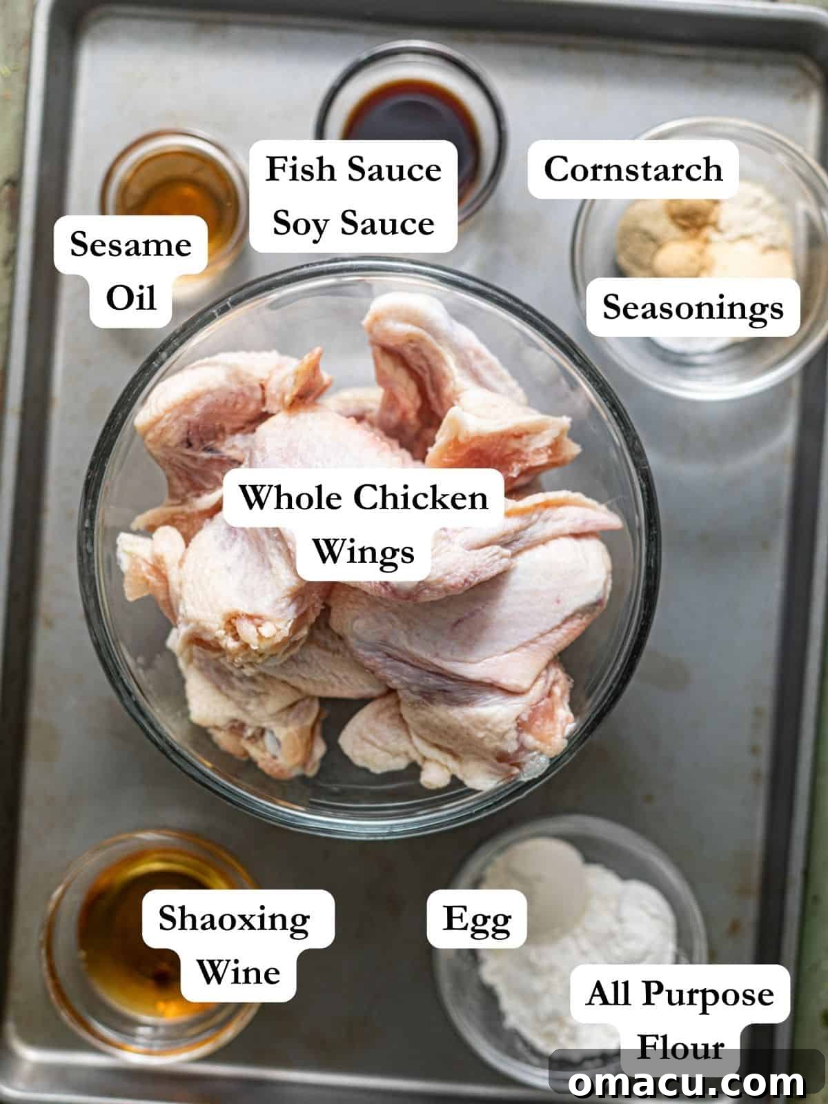 A vibrant display of ingredients meticulously arranged for making deep-fried Chinese wings, including whole chicken wings, flour, cornstarch, white pepper, an egg, sesame oil, garlic powder, onion powder, Shaoxing wine, fish sauce, soy sauce, salt, and black pepper.