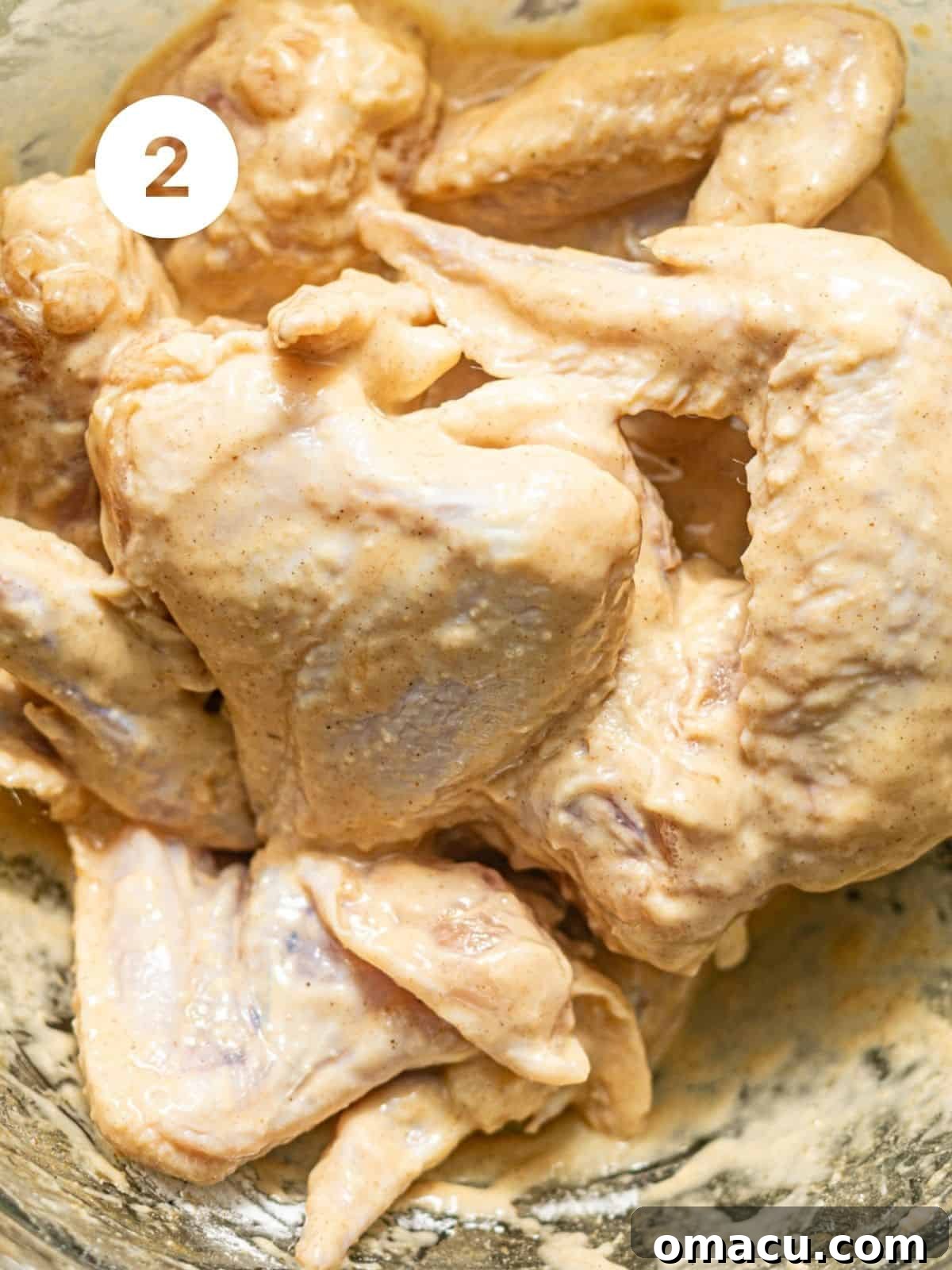 Marinated chicken wings in a bowl, now coated with an additional layer of cornstarch and flour, along with seasonings, creating a sticky, ready-to-fry texture.