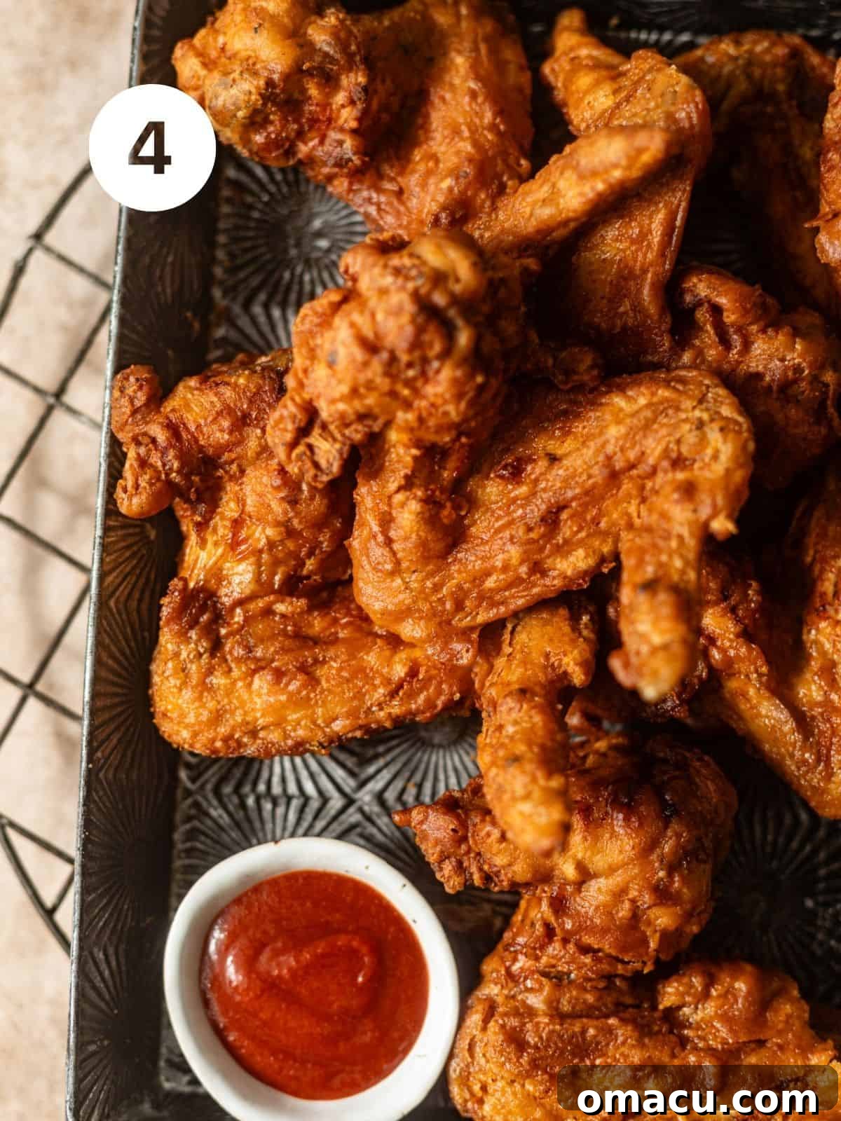 A serving tray laden with perfectly crispy Chinese fried chicken wings, accompanied by a small bowl of fiery sriracha sauce for dipping.