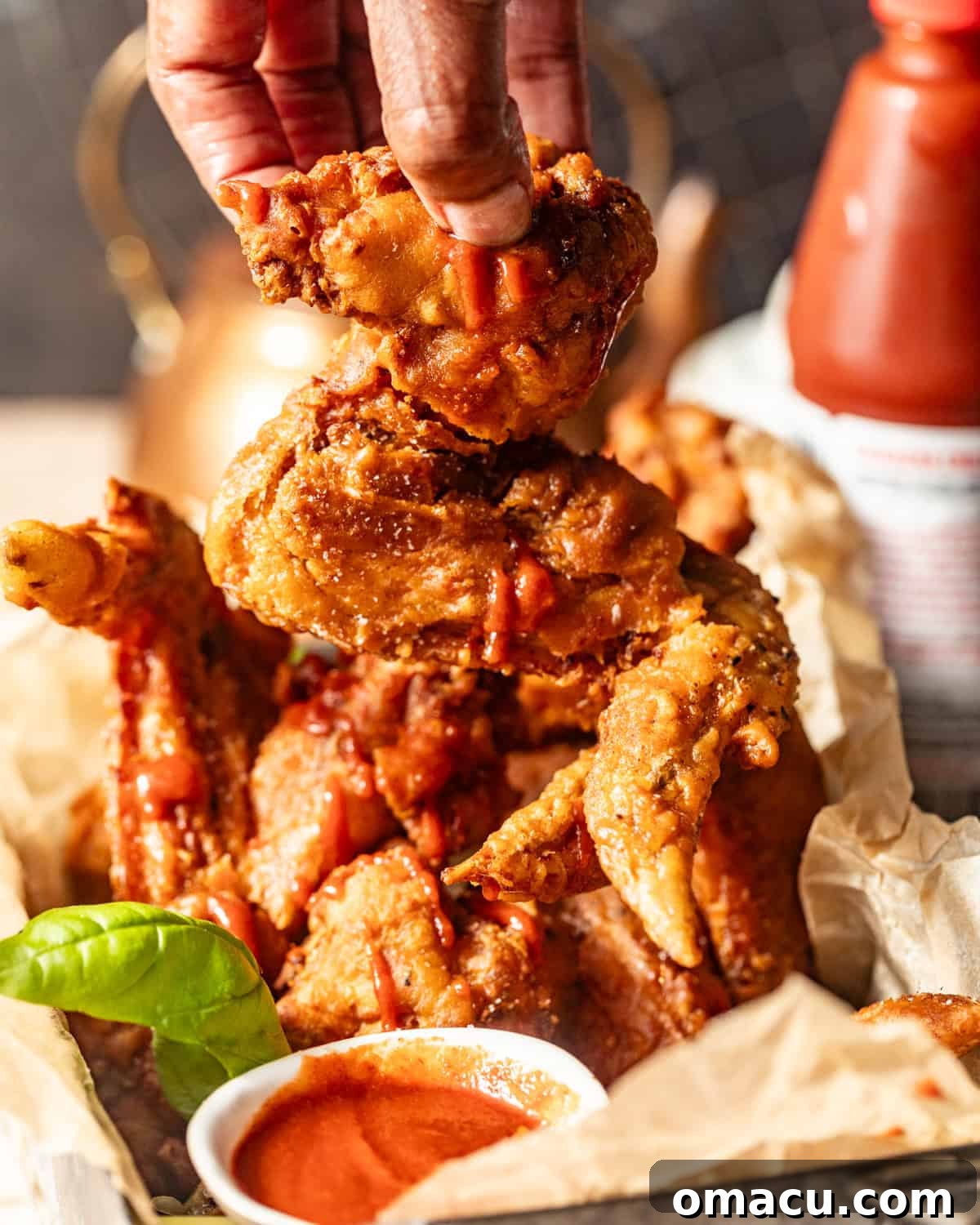 A hand expertly dipping a piece of golden-fried chicken into a savory sauce, highlighting the perfect crispiness of the wing.