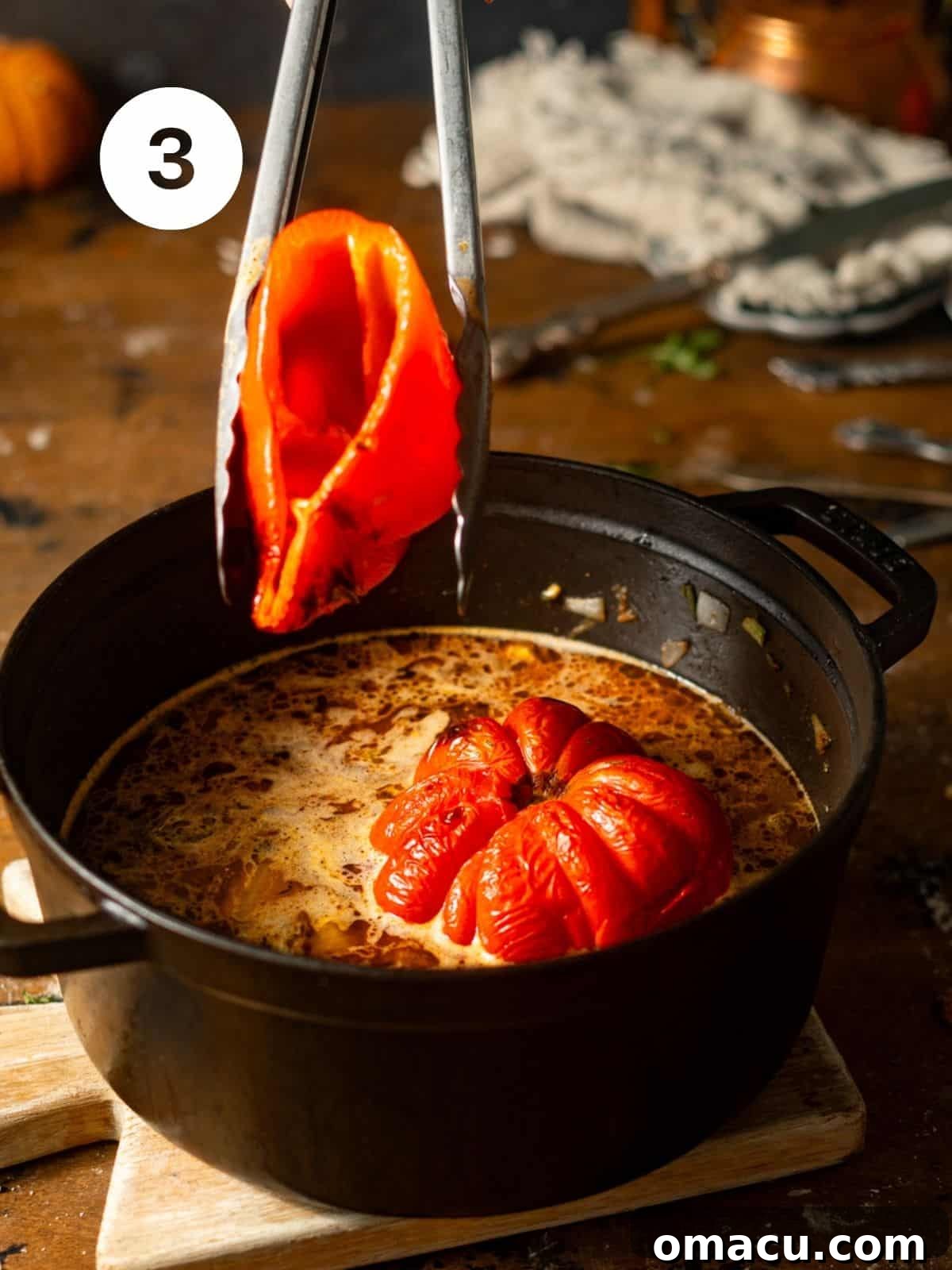 The beautifully charred roasted red peppers and tomatoes being gently added into the dutch oven, joining the aromatic sautéed vegetables and chicken broth to simmer and merge flavors.