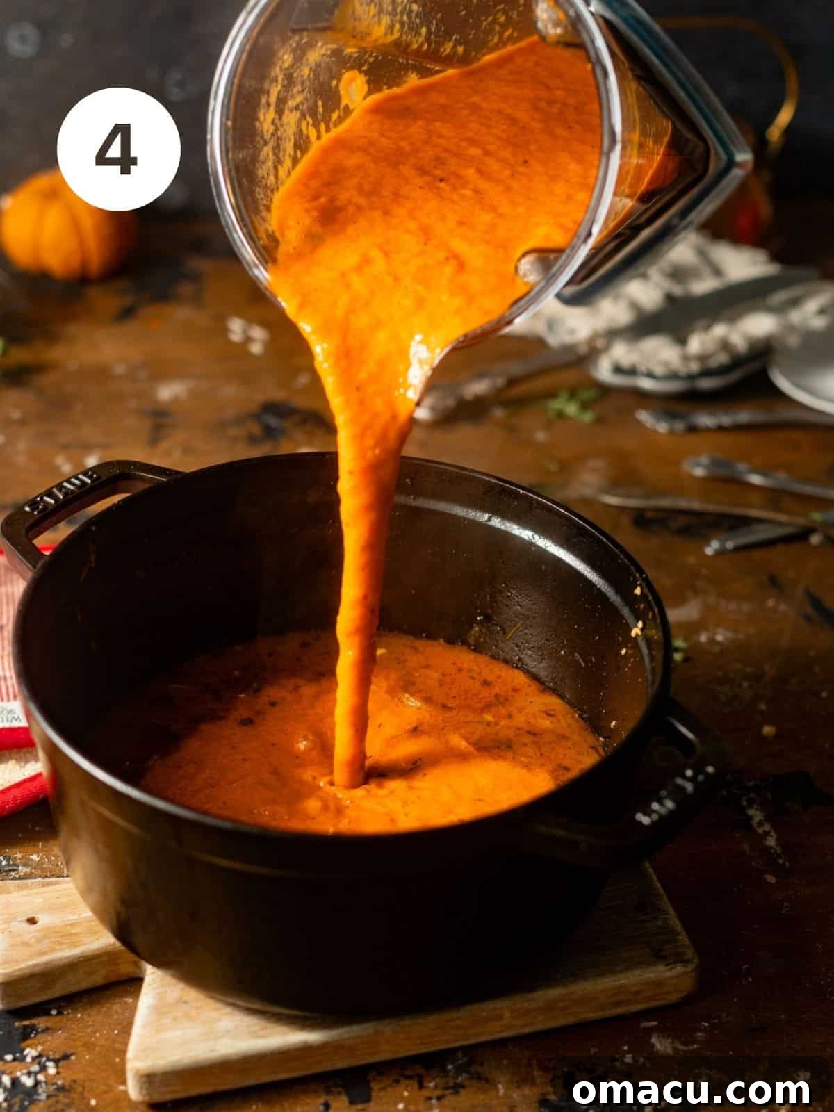 Smooth, blended red pepper and gouda soup being carefully poured back into the large pot from a blender, ready for the final creamy additions and simmering.