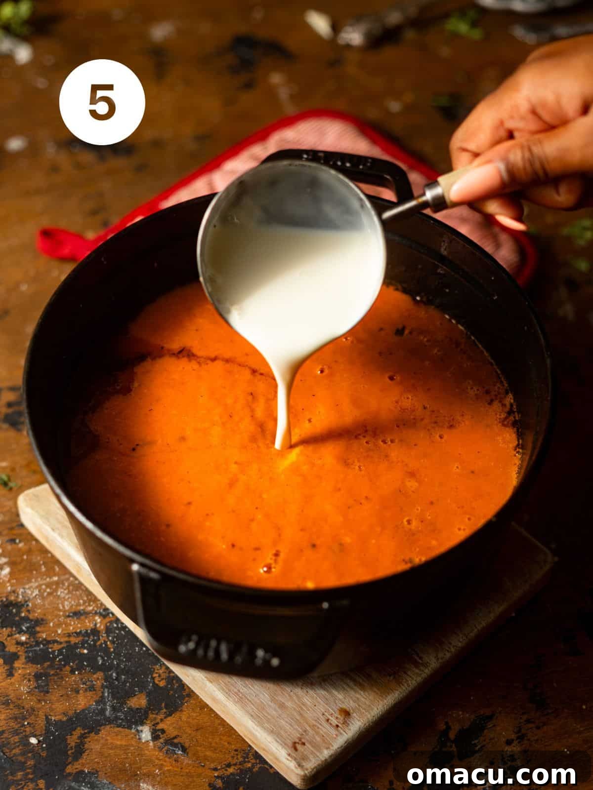 A generous pour of heavy cream and a handful of shredded smoked gouda cheese being added into the rich, blended red pepper soup in the pot, ready to create a truly decadent and creamy finish.