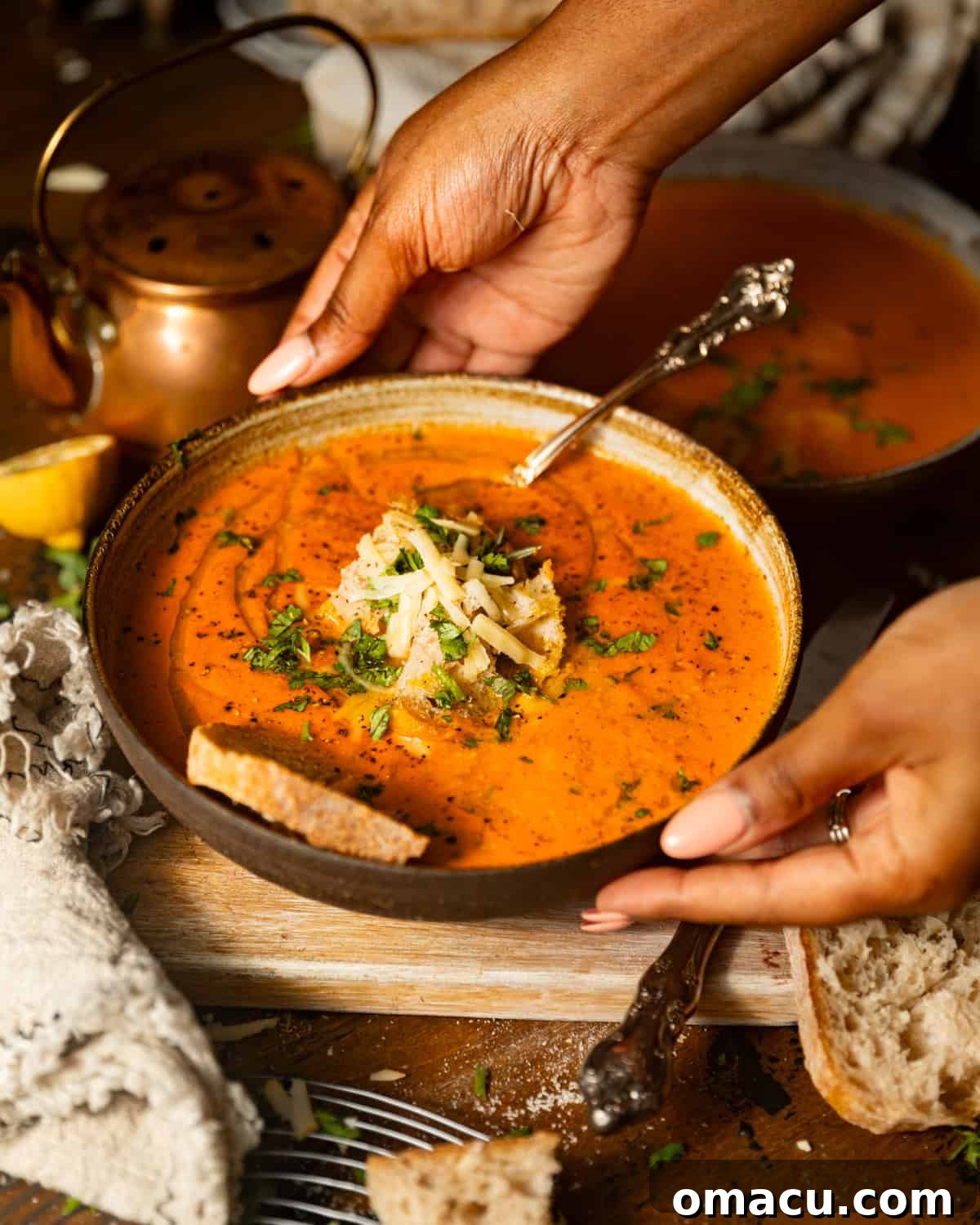 A pair of hands gently holding a warm bowl of creamy Roasted Red Pepper and Smoked Gouda Soup, garnished with a swirl of cream and fresh herbs, suggesting comfort and warmth.