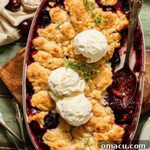 Cherry cobbler in a baking dish with a spoon and ice cream on top.