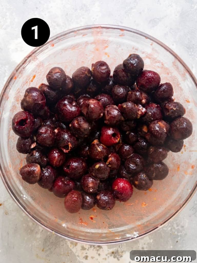 Frozen cherries mixed with sugar, cornstarch, lemon juice, and lemon zest in a glass bowl, ready for baking.