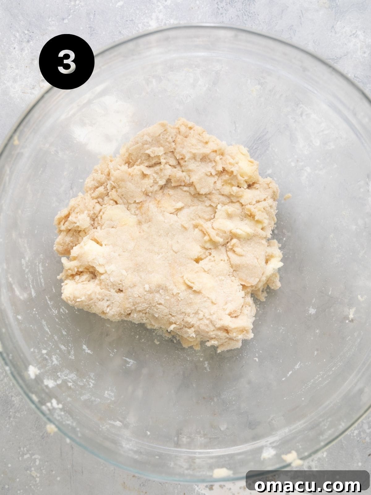 The biscuit topping dough, shaggy but coming together, resting in a bowl before being placed on the cobbler.