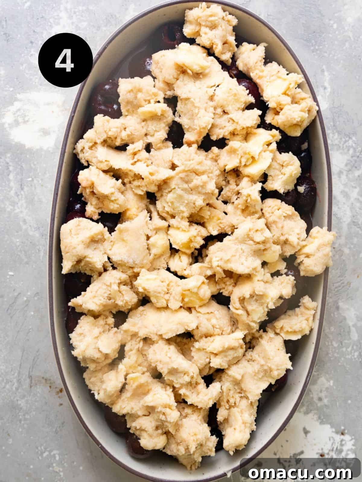 Assembled cherry cobbler in a baking dish, with the biscuit topping dolloped over the cherry filling, ready for baking.