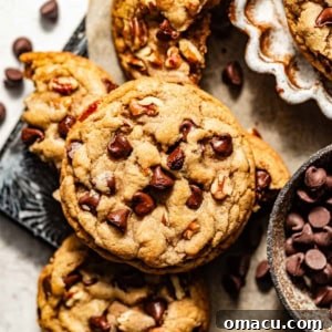 A close-up of a freshly baked banana chocolate chip cookie on parchment paper, surrounded by scattered chocolate chips, highlighting its irresistible texture.