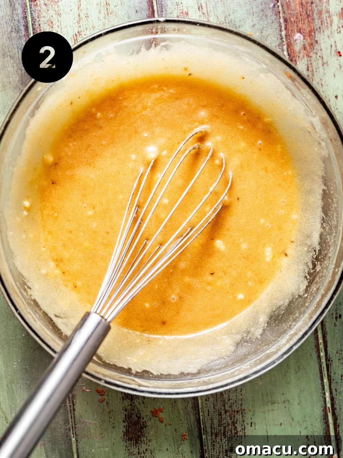 Wet ingredients including mashed bananas, sugars, melted butter, and vanilla extract, whisked together until light and creamy in a bowl.