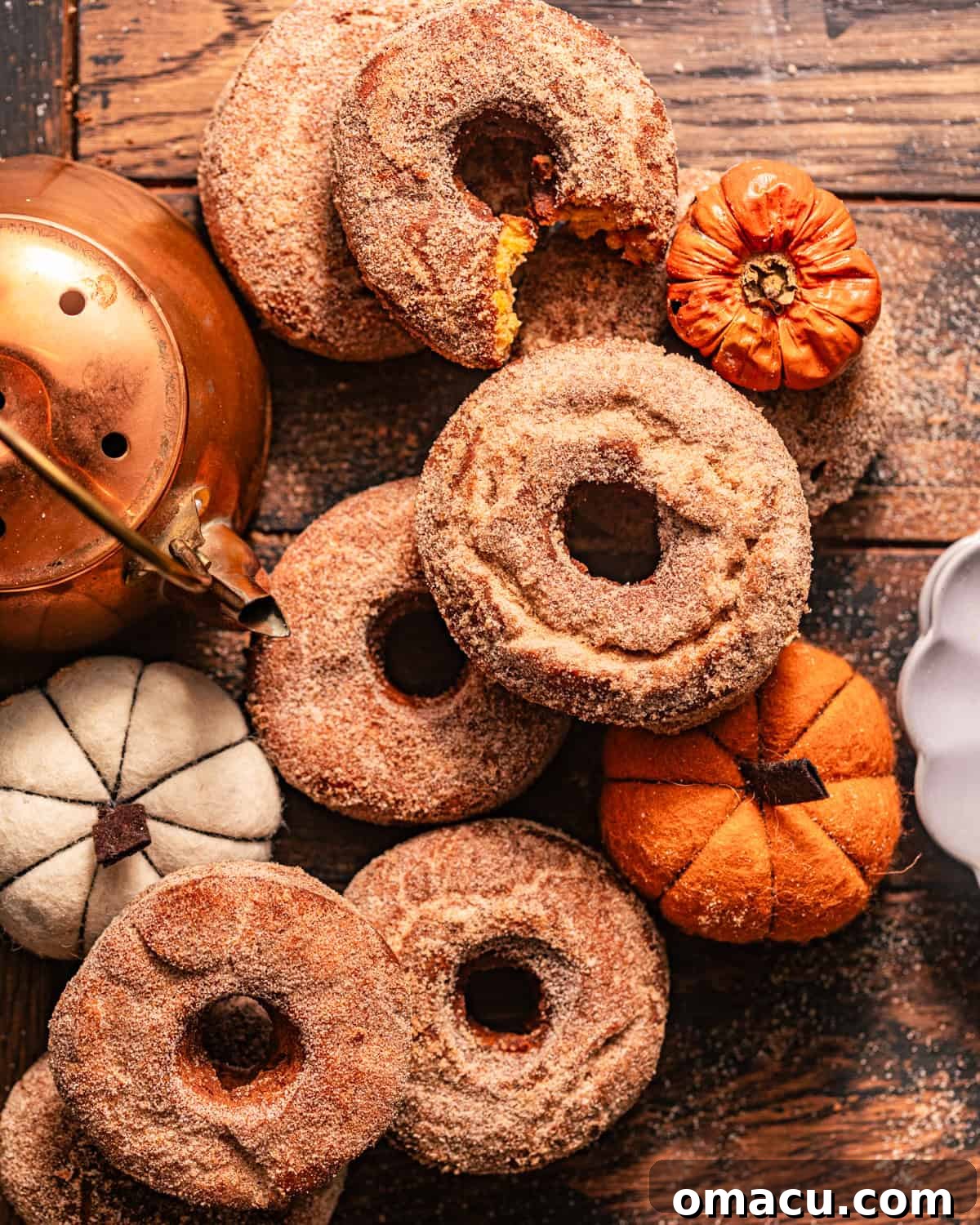 An inviting spread of pumpkin spice donuts on a rustic wooden table, enhanced by decorative mini pumpkins and a classic copper kettle, capturing the essence of fall.