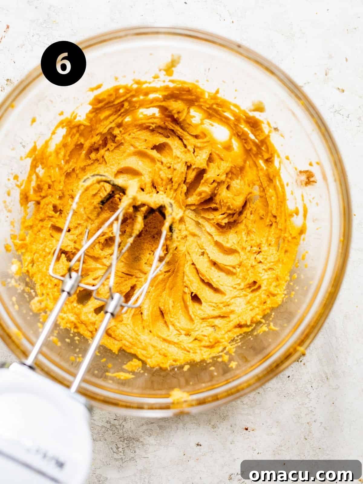 Room temperature butter, brown sugar, egg yolks, and the prepared pumpkin puree are vigorously mixed together using a hand mixer in a large bowl, creating a rich wet batter.
