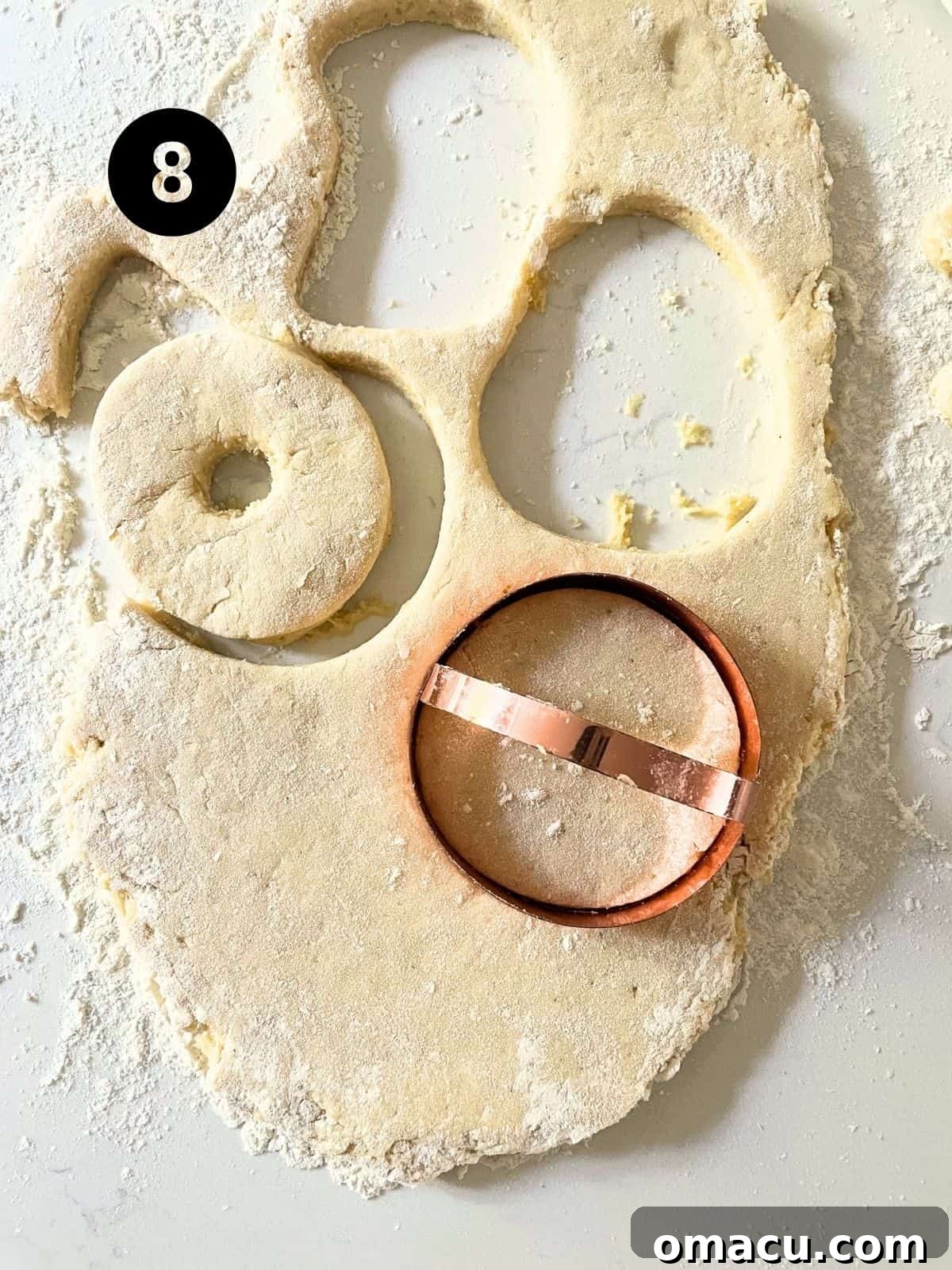 Pumpkin donut dough rolled out onto a floured surface, with donut shapes being cut out using a round cutter, showcasing the preparation process.