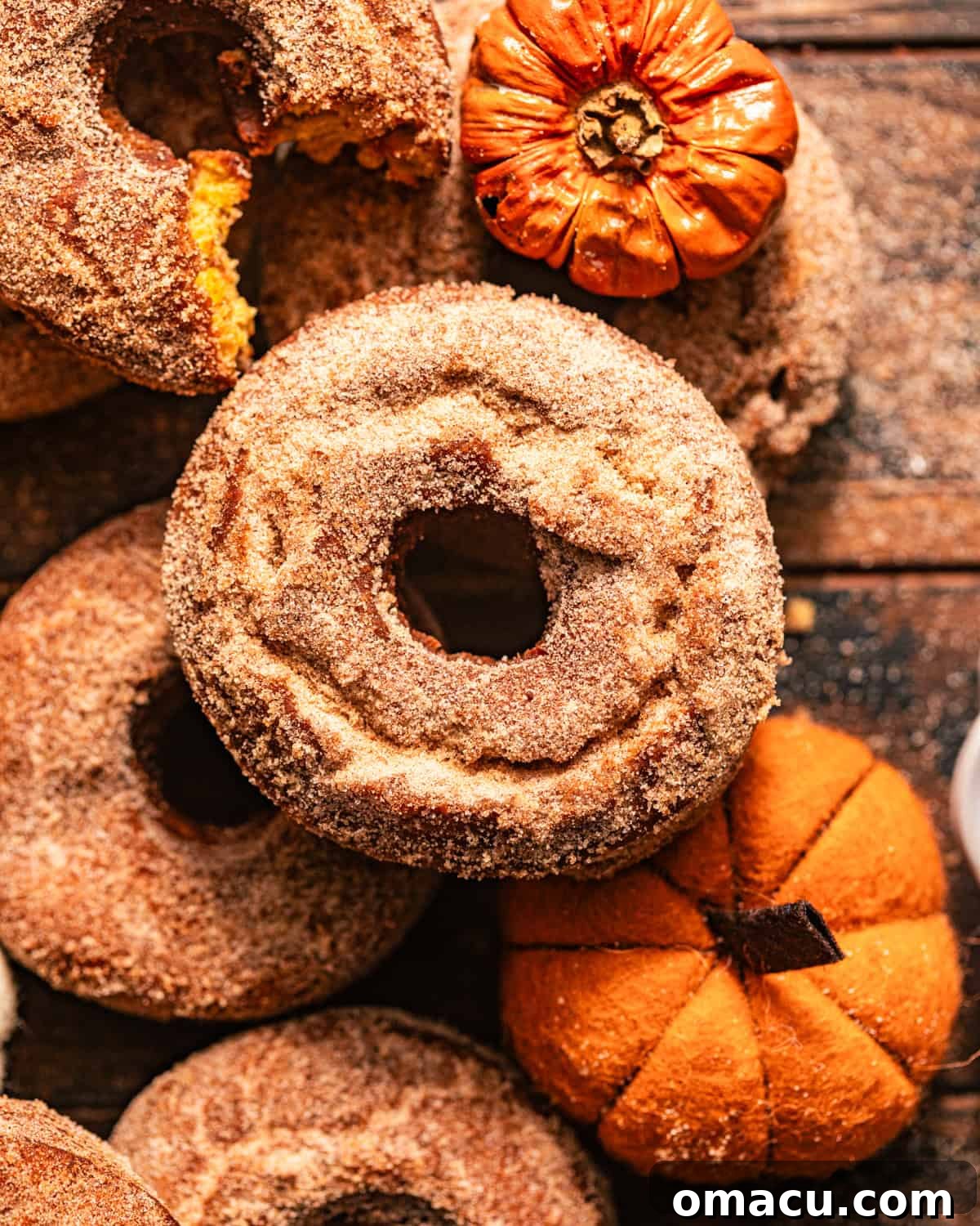 Golden brown pumpkin spice donuts coated in a generous layer of cinnamon sugar, arranged on a rustic wooden table.