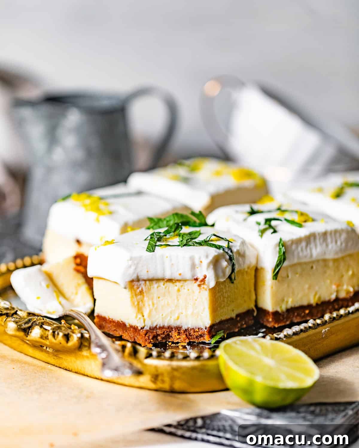 Golden serving tray with perfectly sliced key lime pie bars, garnished with fresh lime zest and vibrant chopped mint leaves, evoking a refreshing tropical dessert.