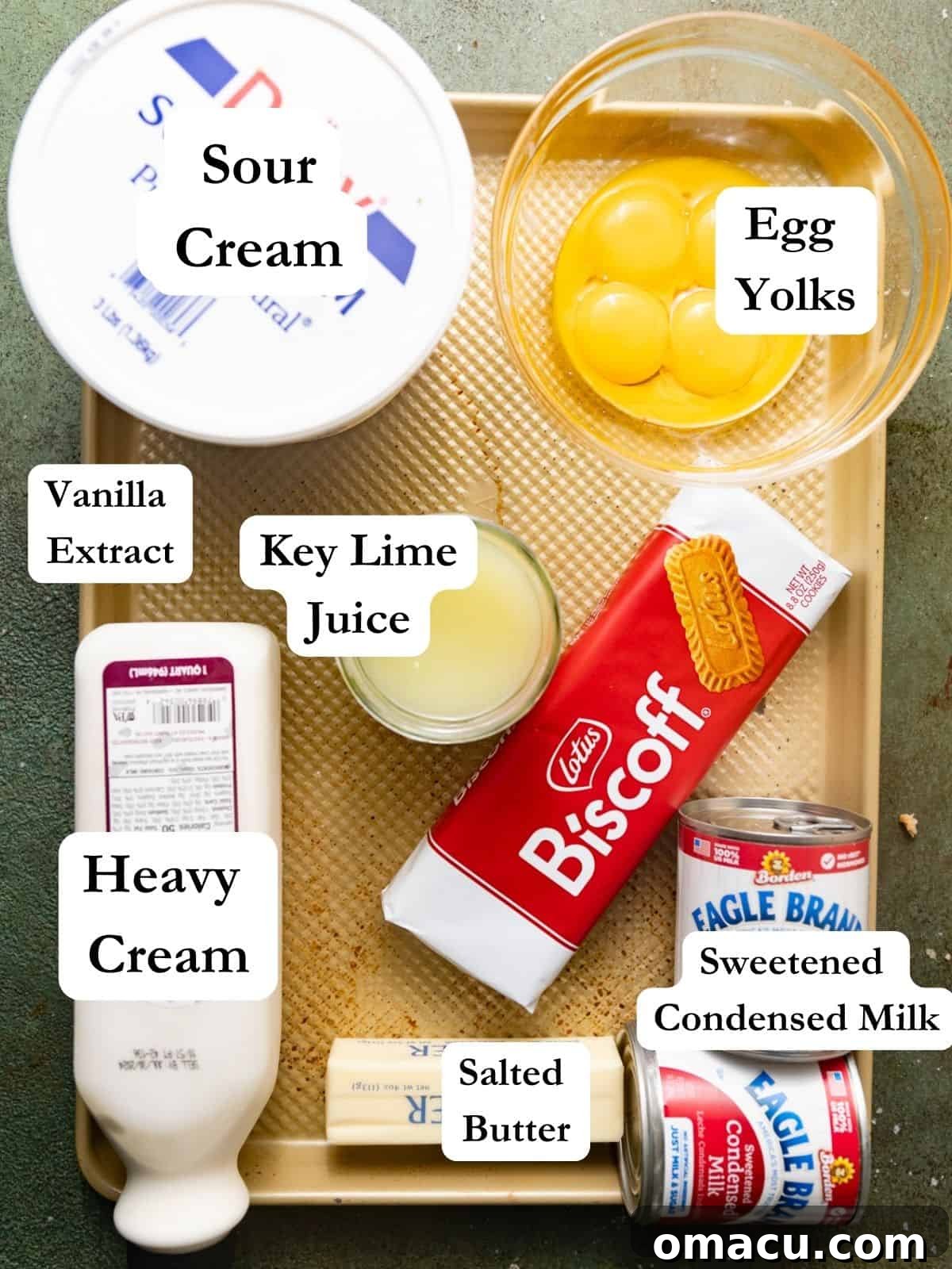 A beautifully arranged selection of fresh ingredients required to make key lime pie bars, including vibrant key lime juice, separated egg yolks, sweetened condensed milk, heavy cream, rich sour cream, melted butter, vanilla extract, and crisp biscoff cookies.