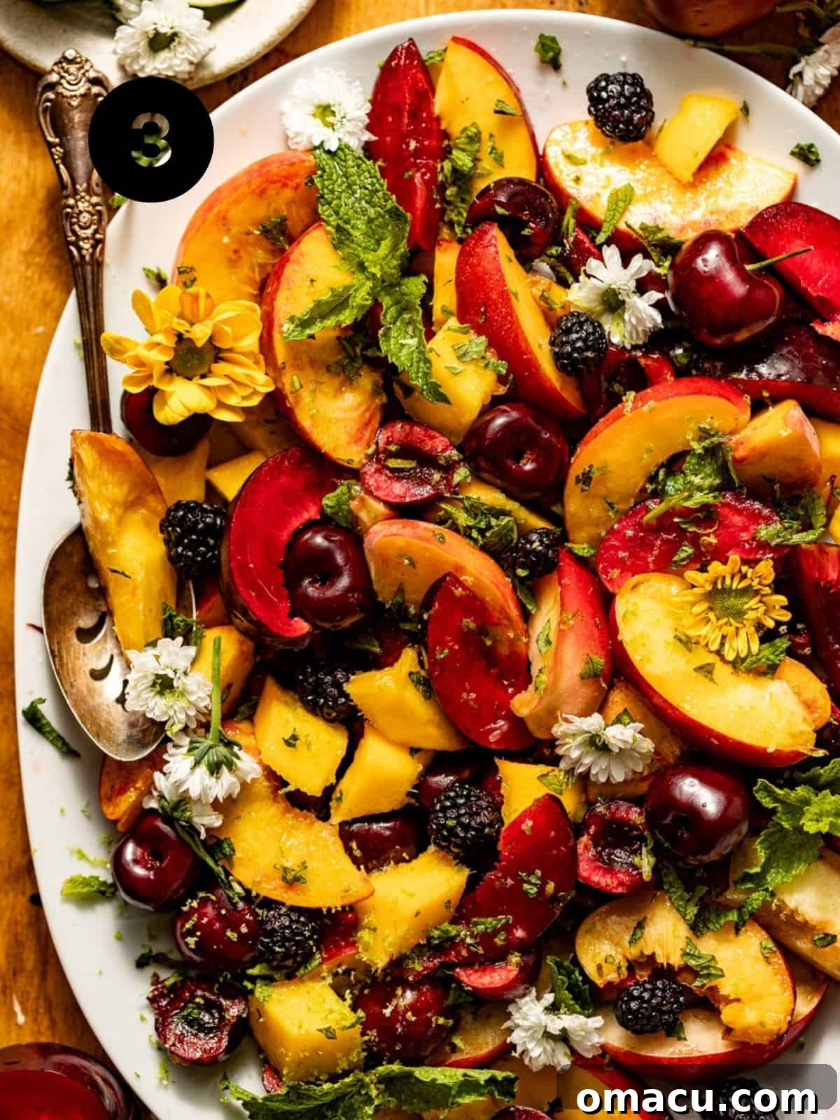 A beautifully assembled stone fruit salad showcased in a white serving bowl, topped with vibrant fresh mint and citrus zest, with a serving spoon gently resting among the colorful fruits, indicating it's ready to be savored.