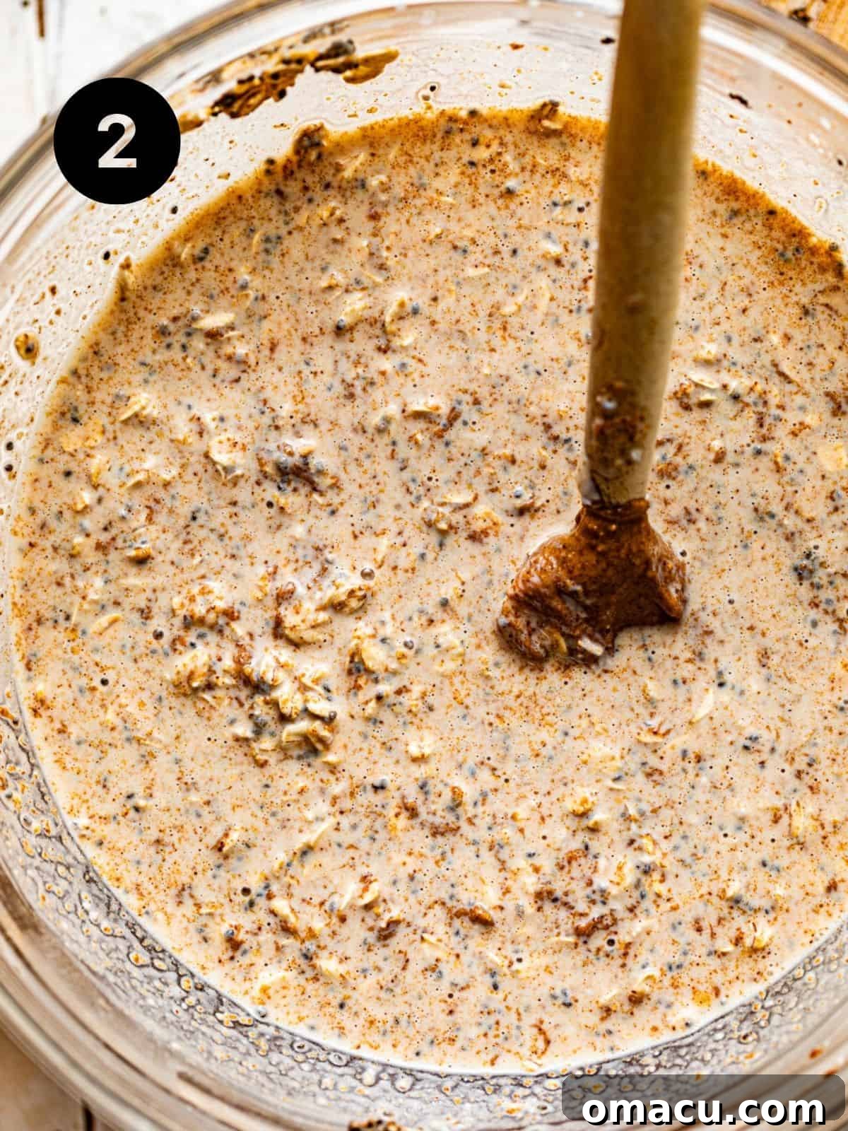 All the overnight oats ingredients, including rolled oats, almond butter, and cinnamon, are thoroughly mixed together in a bowl, creating a creamy and homogenous mixture before chilling.