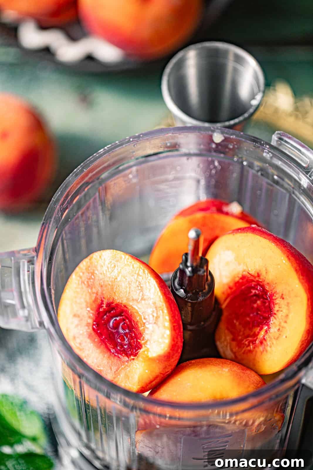 Freshly sliced peaches being added to a food processor, ready for blending into the cocktail base.