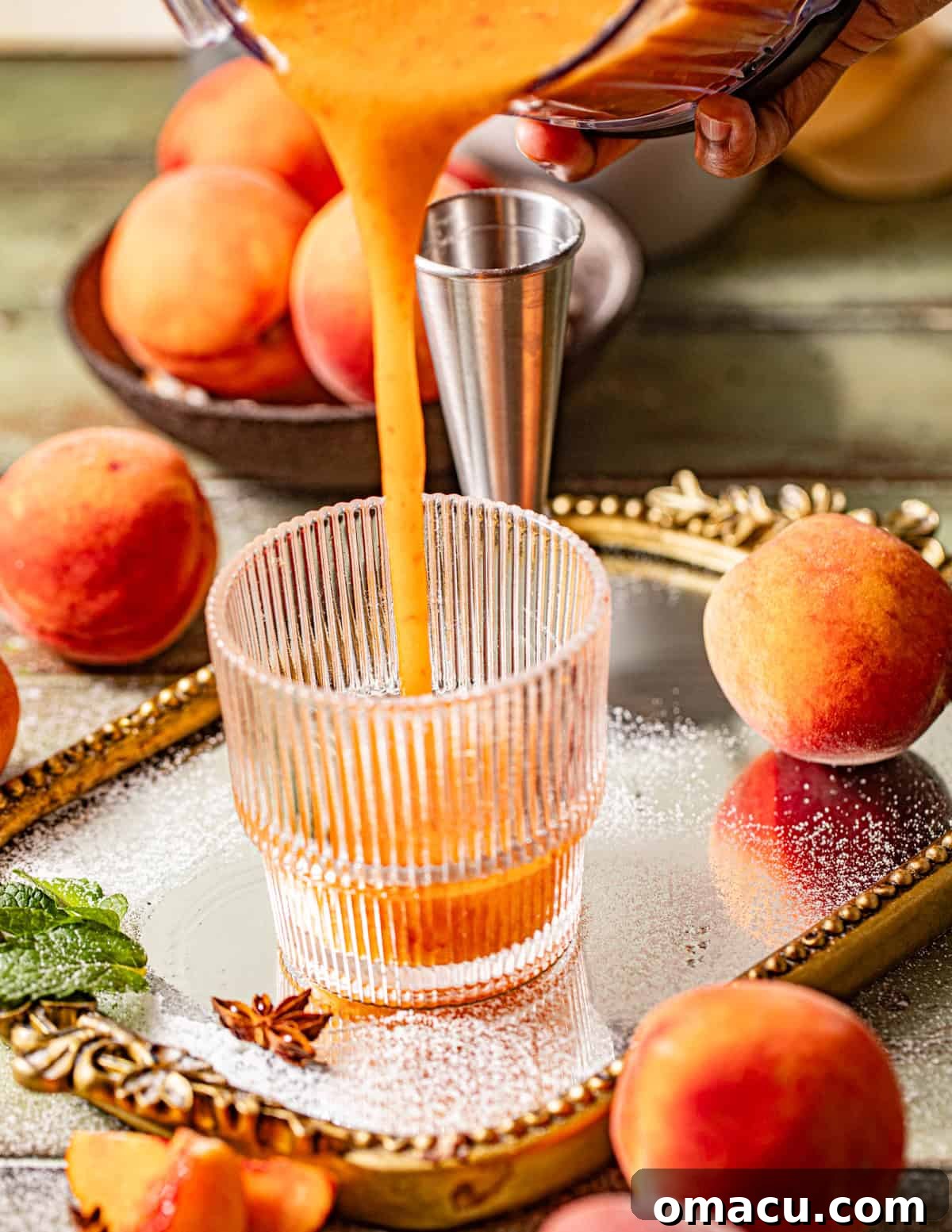 A smooth peach bourbon cocktail mixture being carefully poured from a food processor into a waiting cocktail glass, ready for enjoyment.